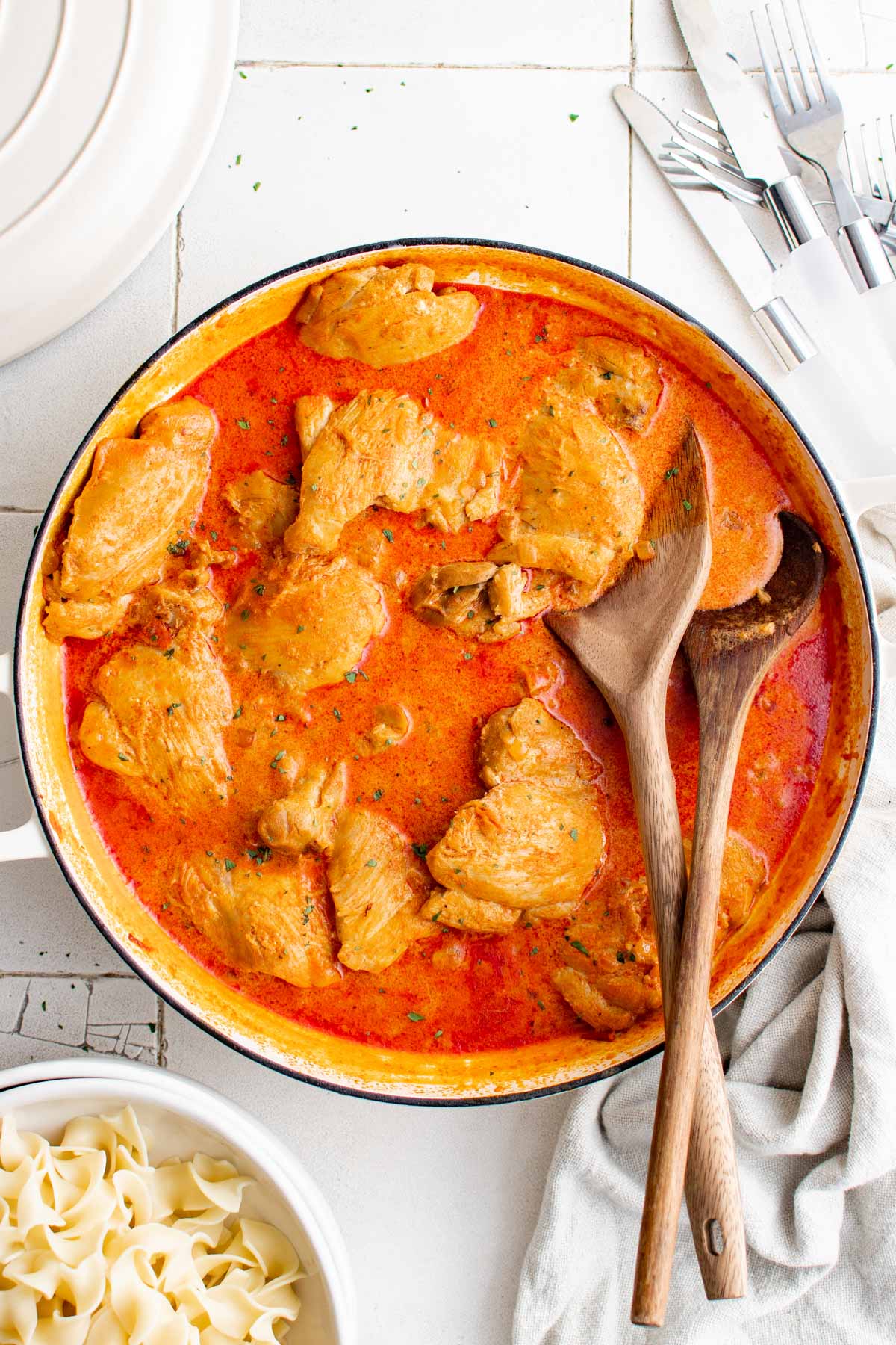 Chicken thighs in a tomato based sauce in a pan with 2 wooden spoons.