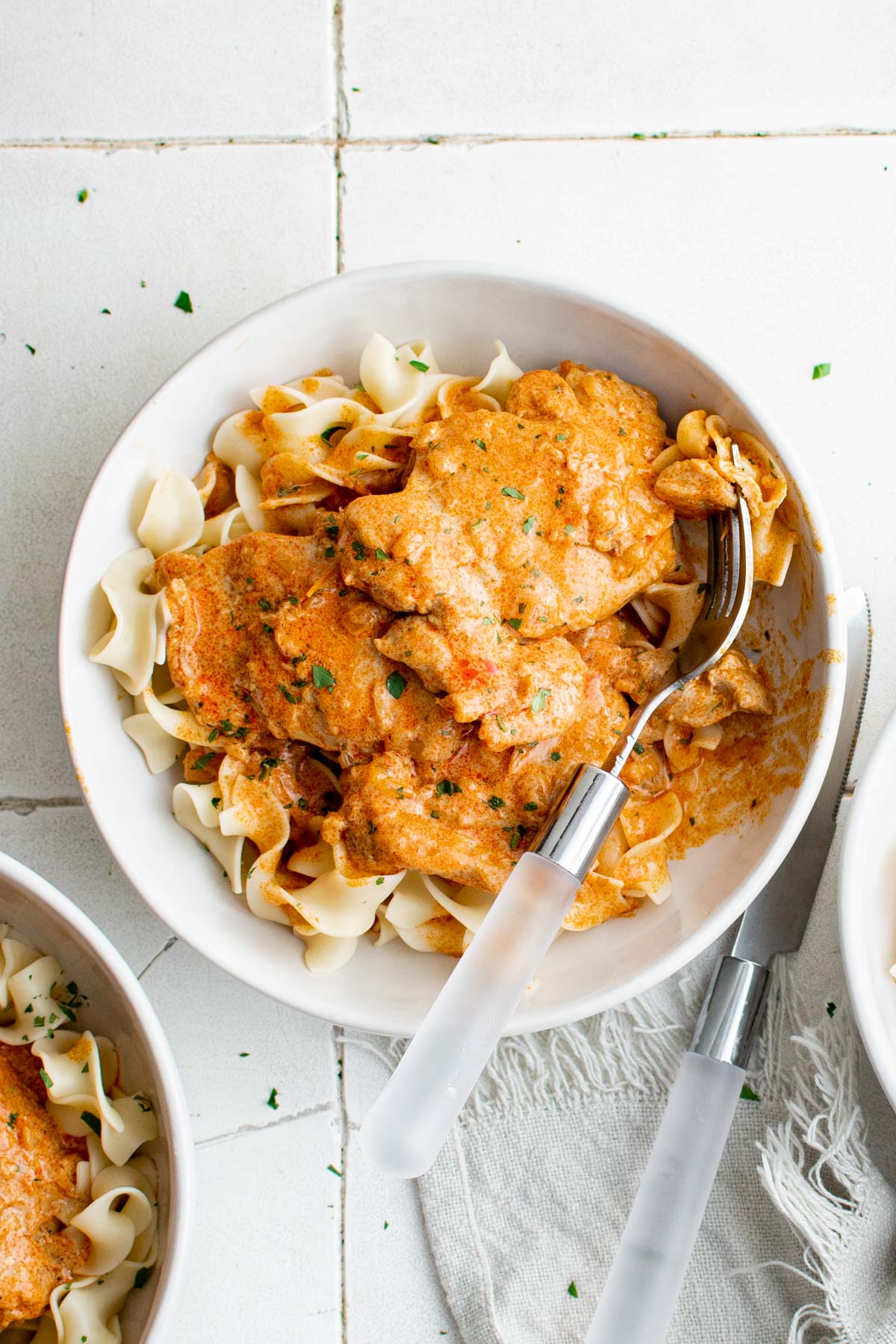 Chicken paprikash in a white bowl with egg noodles and a fork.