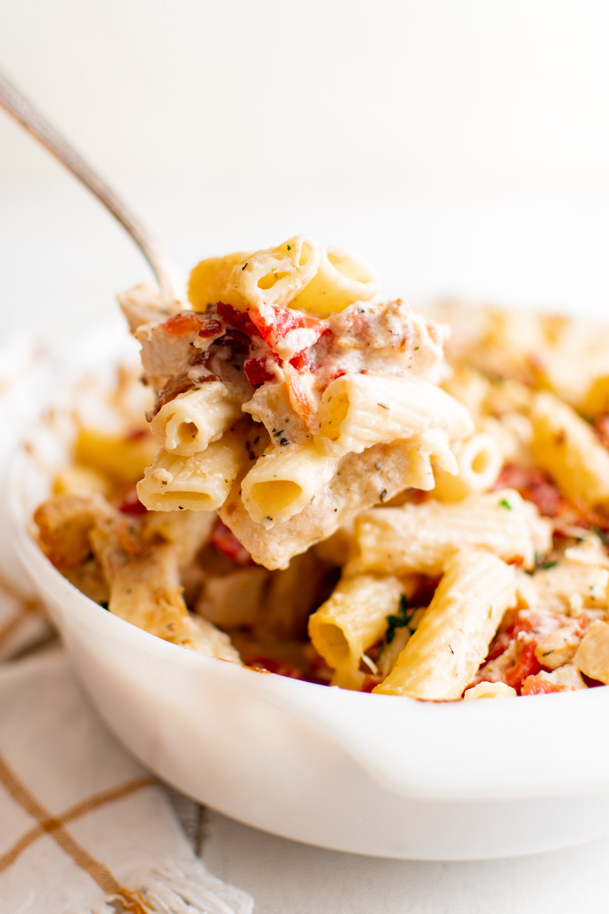 Bowl of pasta with cheese sauce, bacon and chicken and a spoon.
