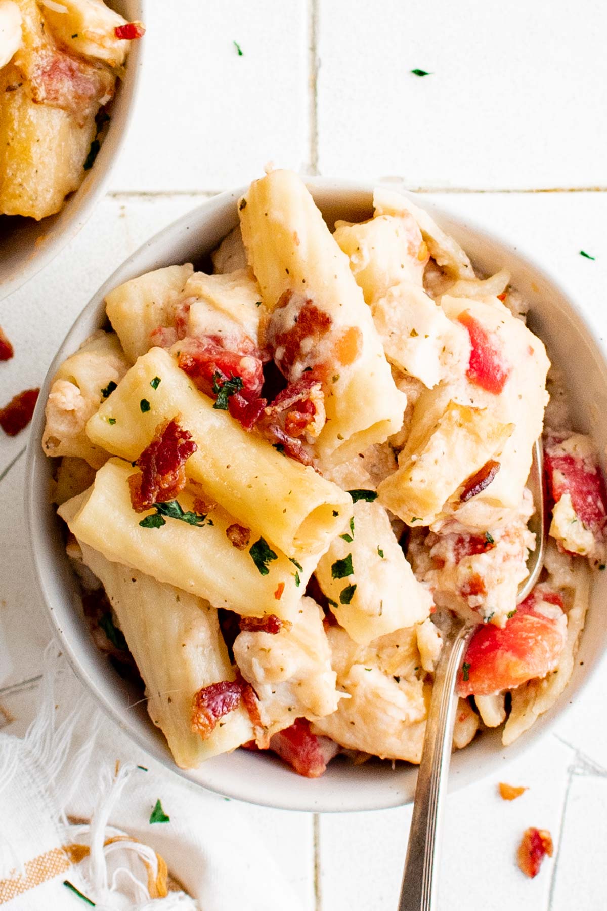 A bowl of pasta with chicken and bacon and a fork.