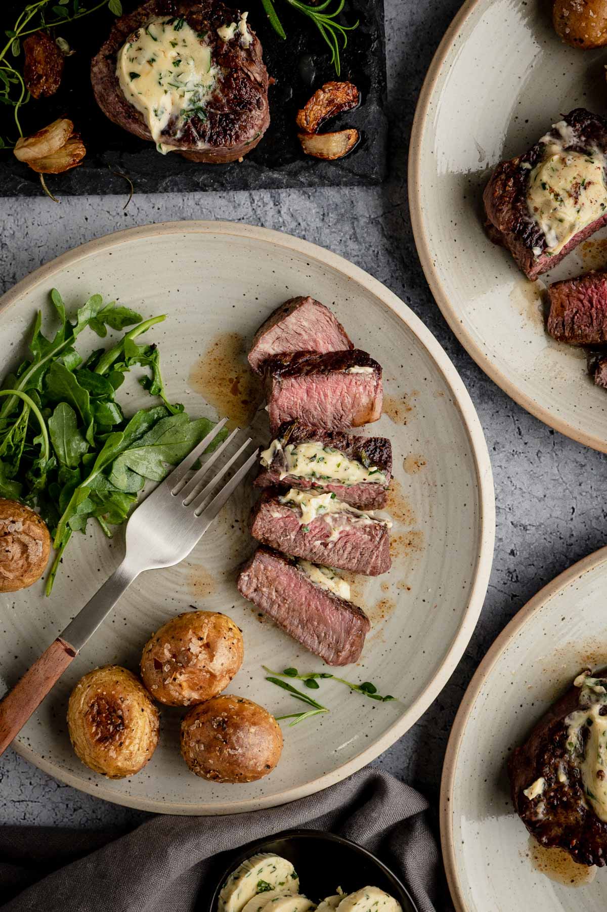 Sliced filet mignon, salad and potatoes on a plate with a fork.