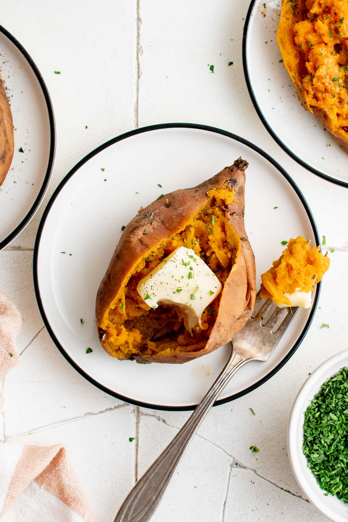 Sweet potato on a white plate, split open with butter and a fork.