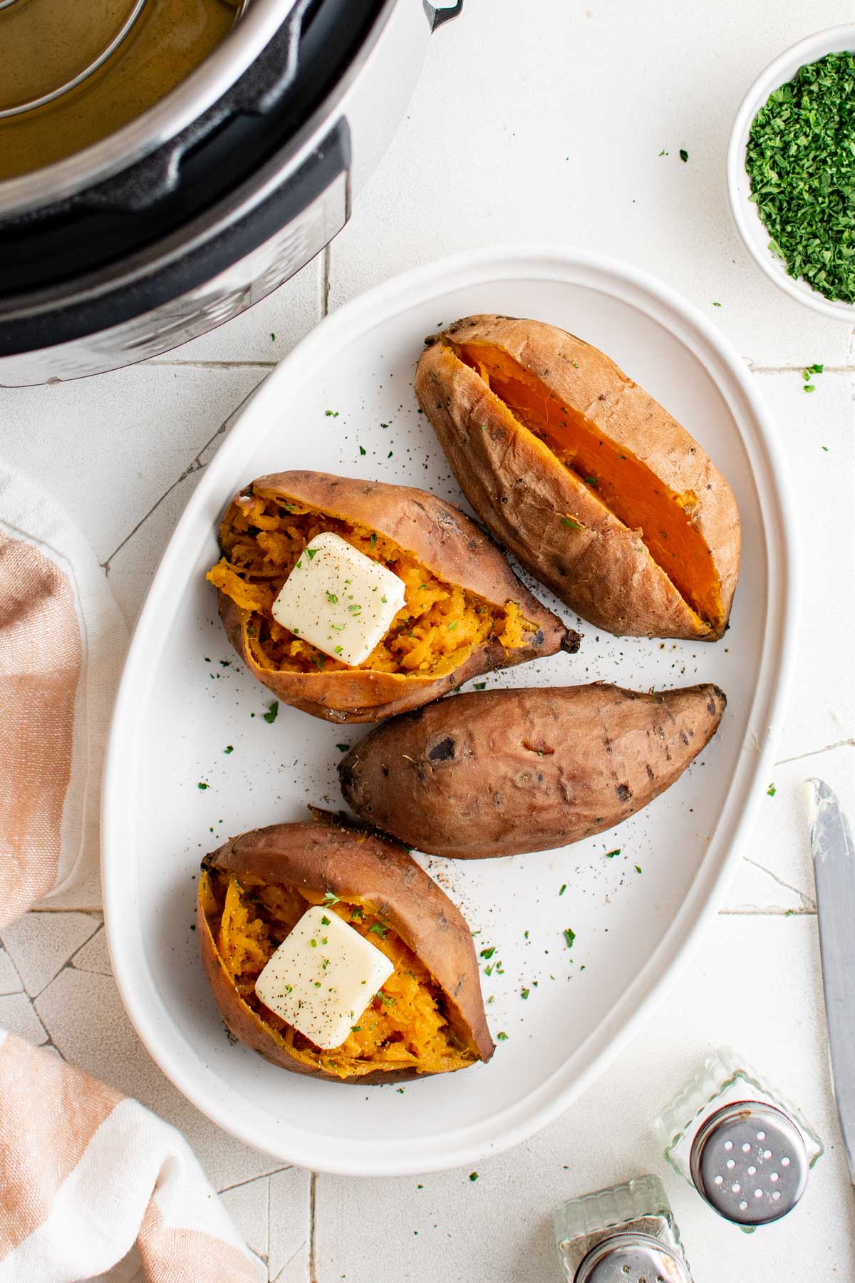 4 sweet potatoes on a white platter, split open with butter and parsley.