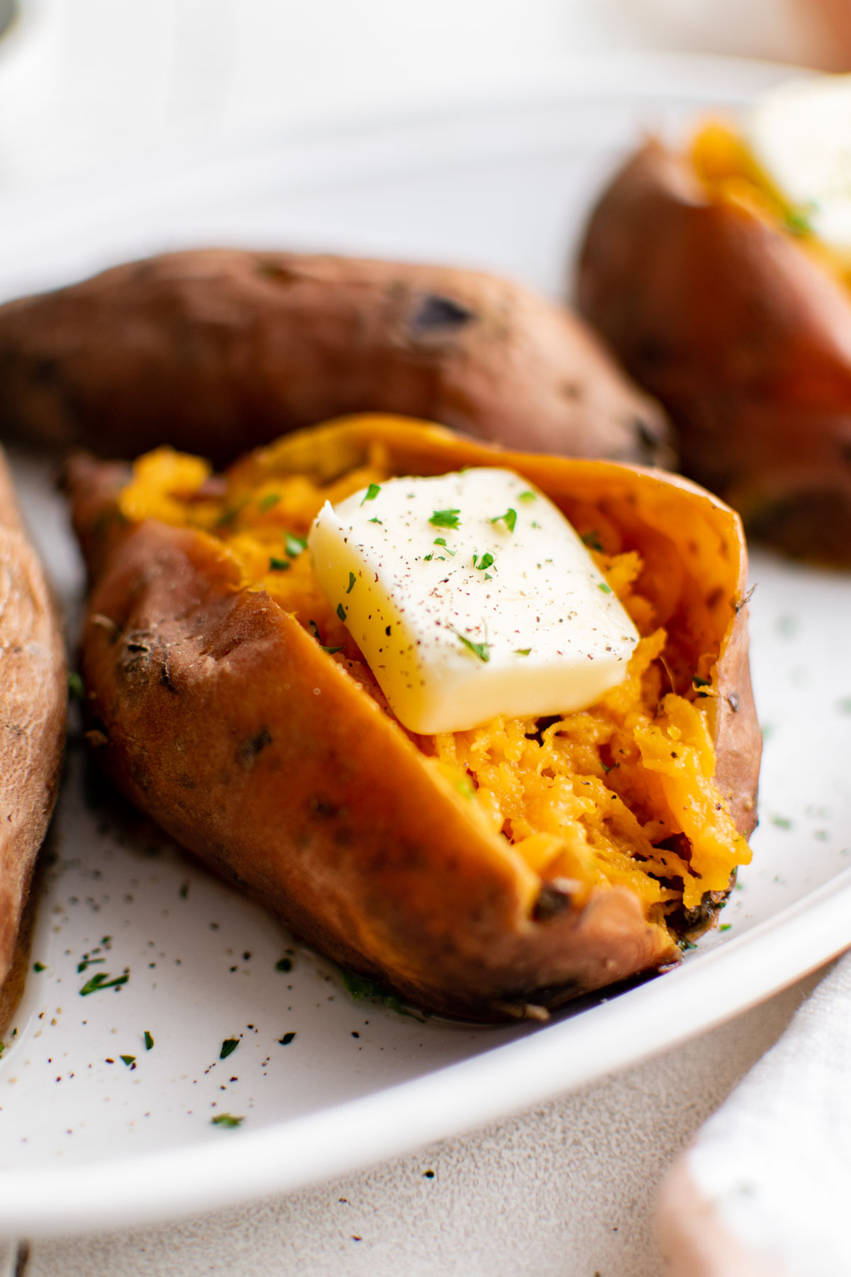 Close up of a sweet potato split open with butter on a white platter.