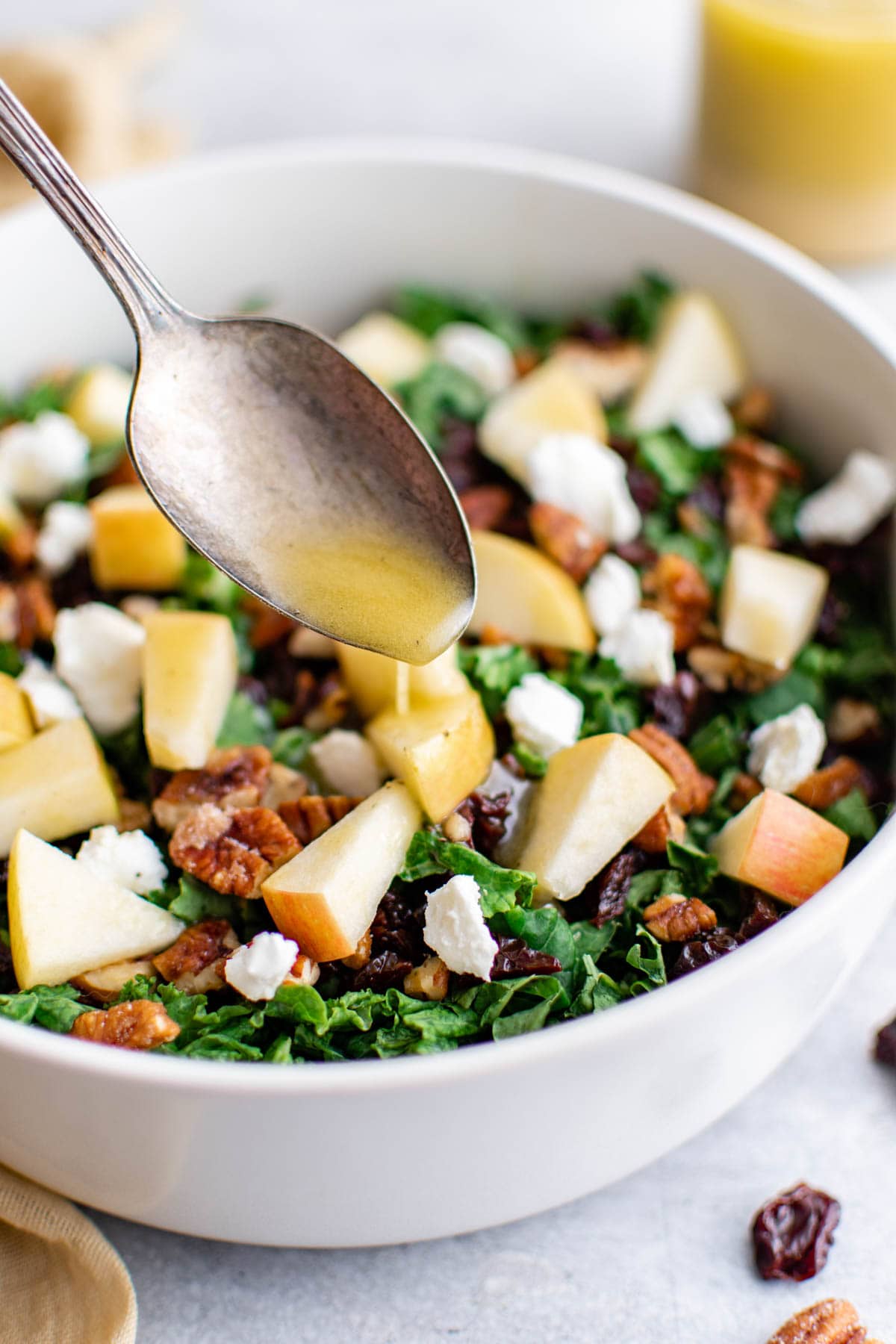 Bowl of kale salad with apples; Champagn vinaigrette drizzled over with a spoon.
