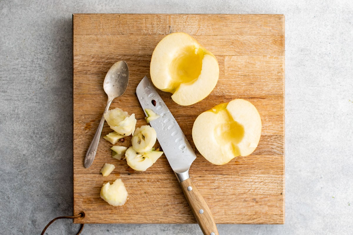 Apple sliced in half, a knife, a cutting board.