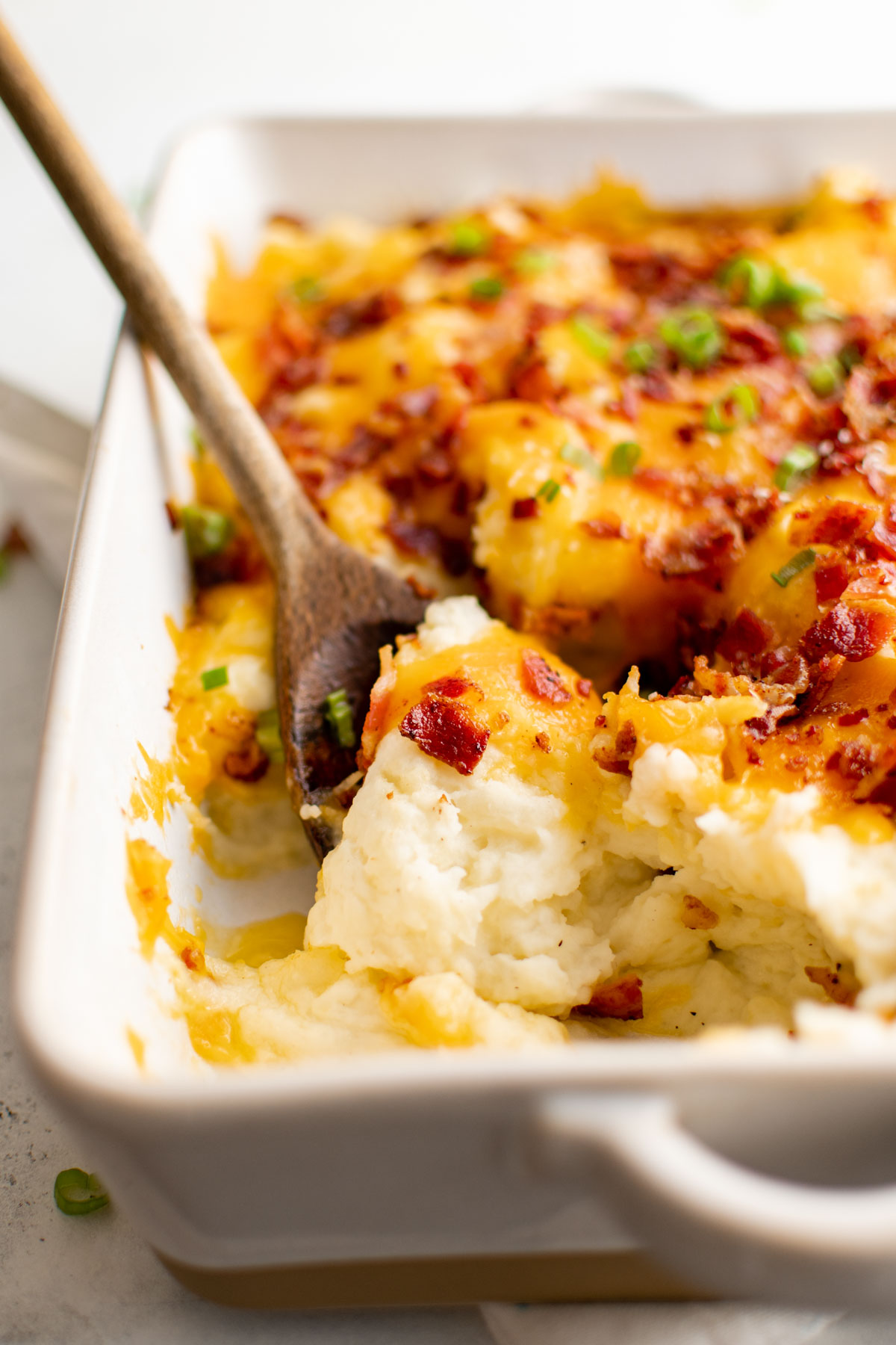Casserole of mashed potatoes with bacon and cheese and a wooden spoon.
