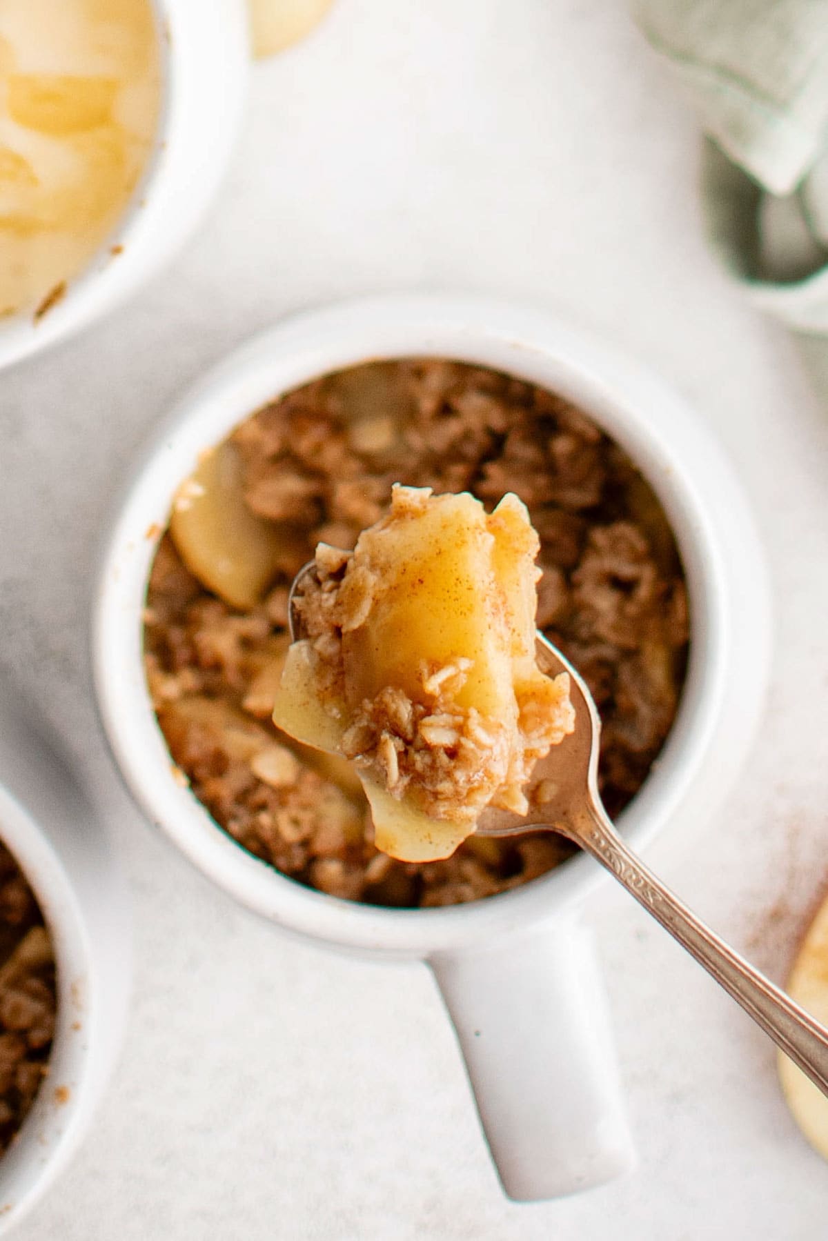 White mug with a silver spoon holding sliced apples and crumb topping.