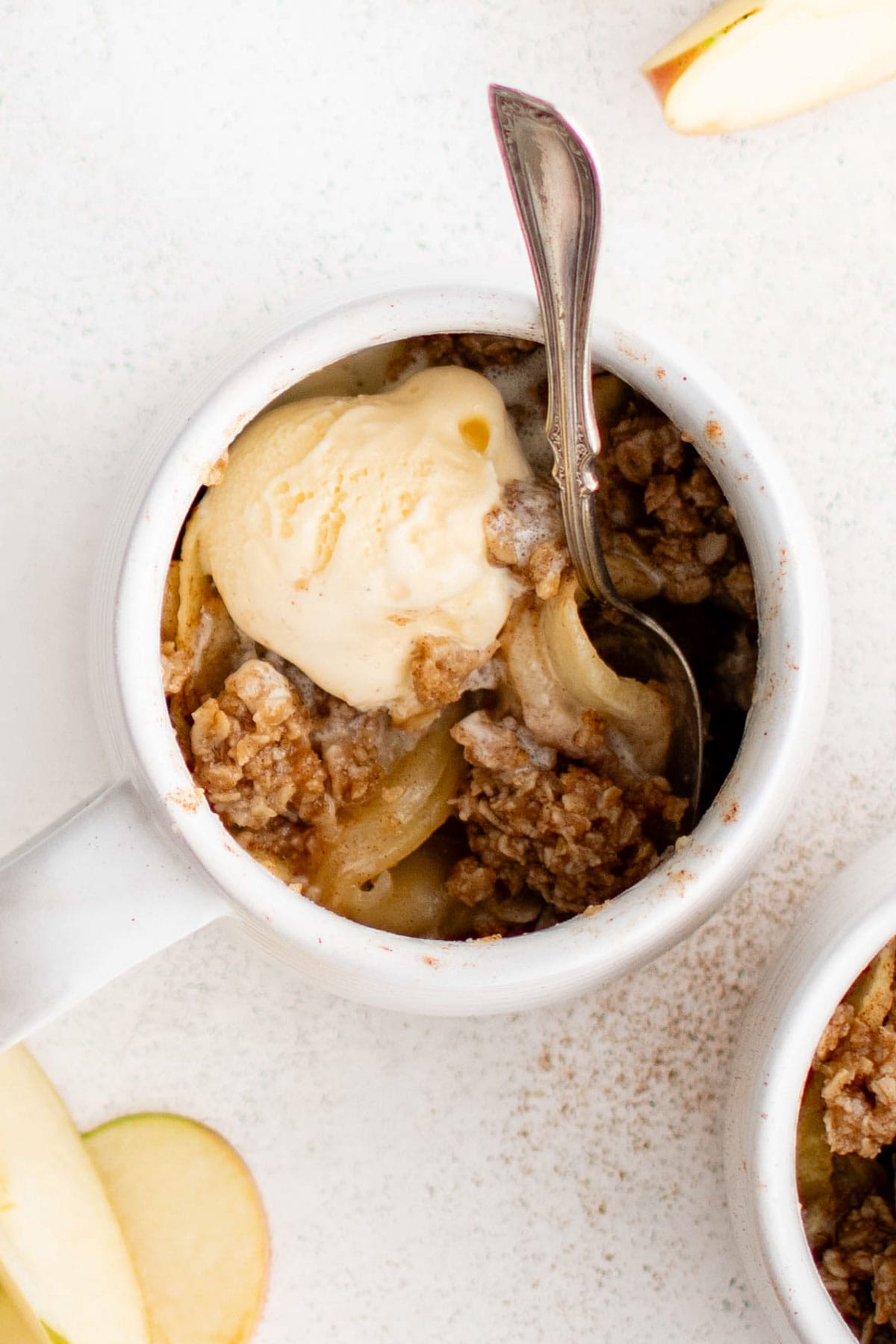 White mug, vanilla ice cream, apple slices with crumble topping, a spoon.