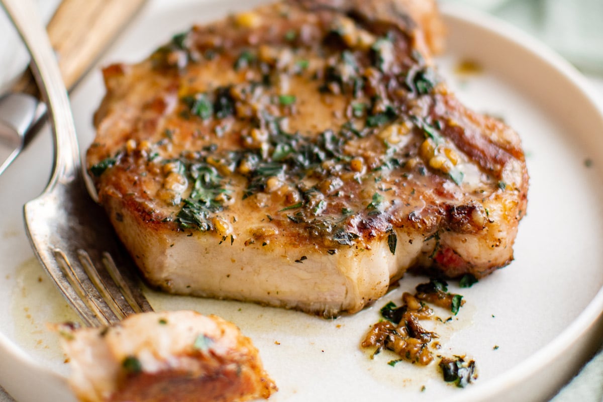 Pork chops on a white plate, with a bite cut and sitting on a fork.