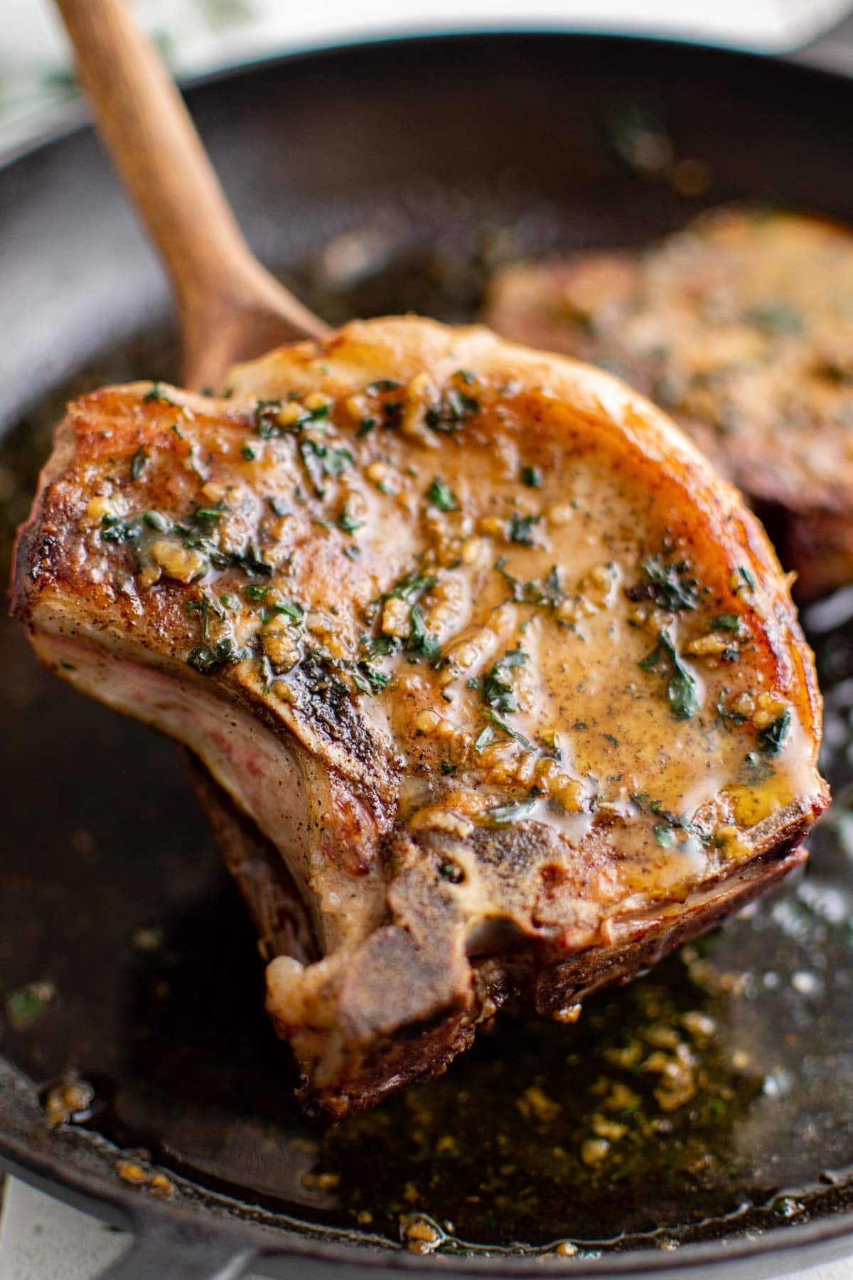 Pork chop and a wooden spatula in a cast iron skillet.