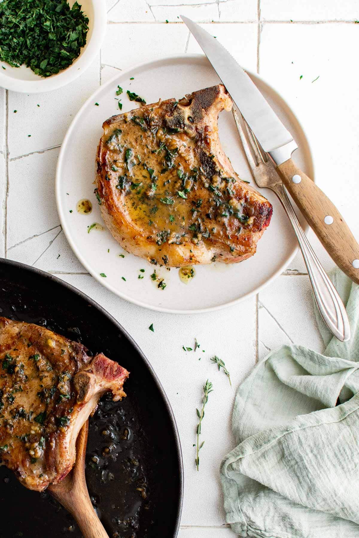 Pork chops with parsley and butter on a plate and in a skillet