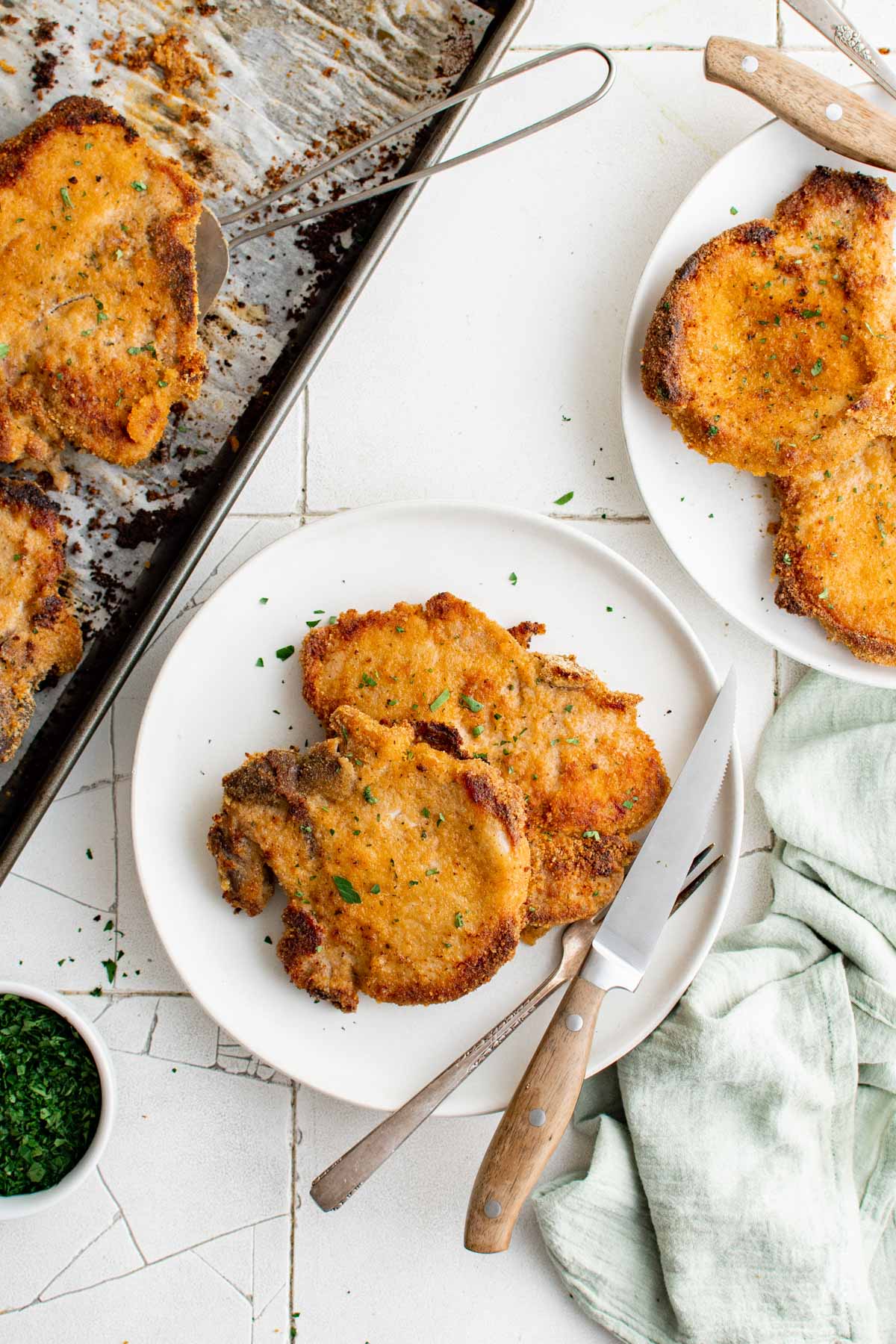 Breaded Baked pork chops on plates with silverware.