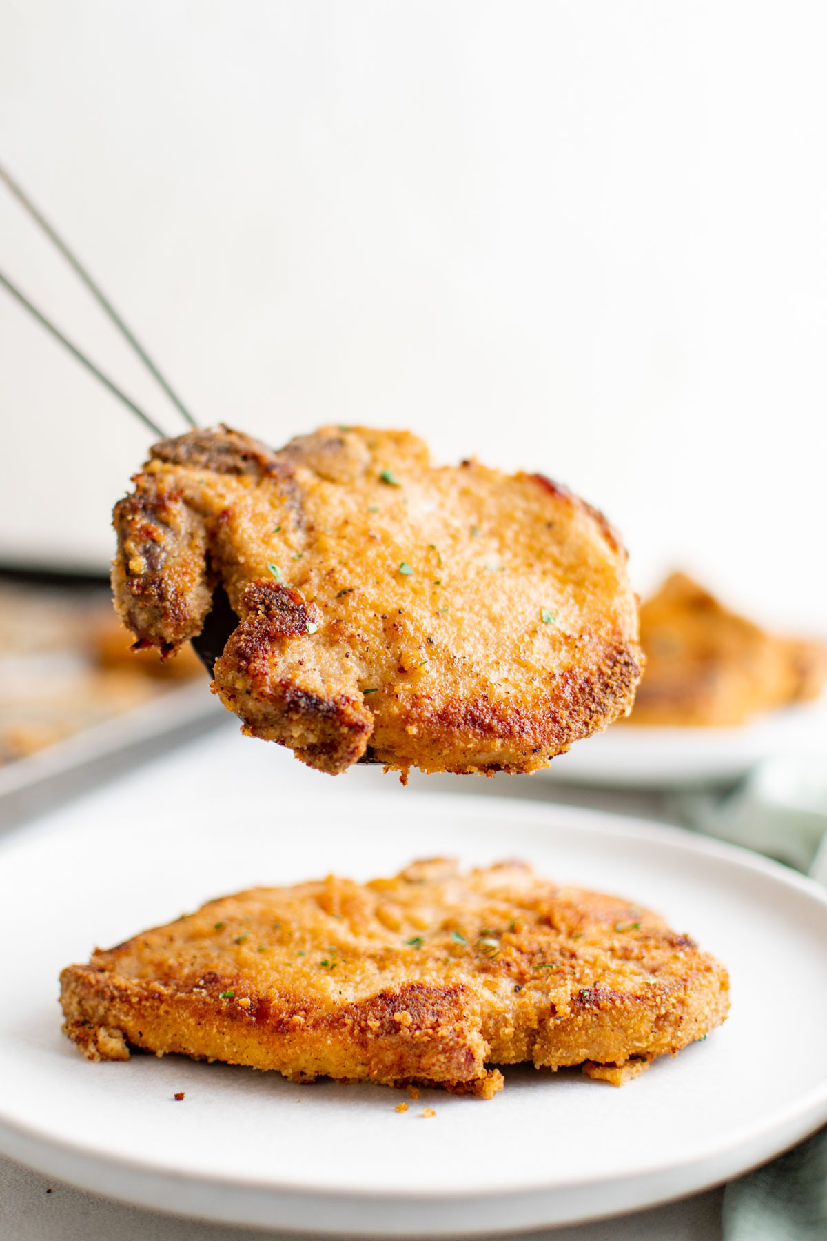A breaded pork chops on a plate and one on a spatula.