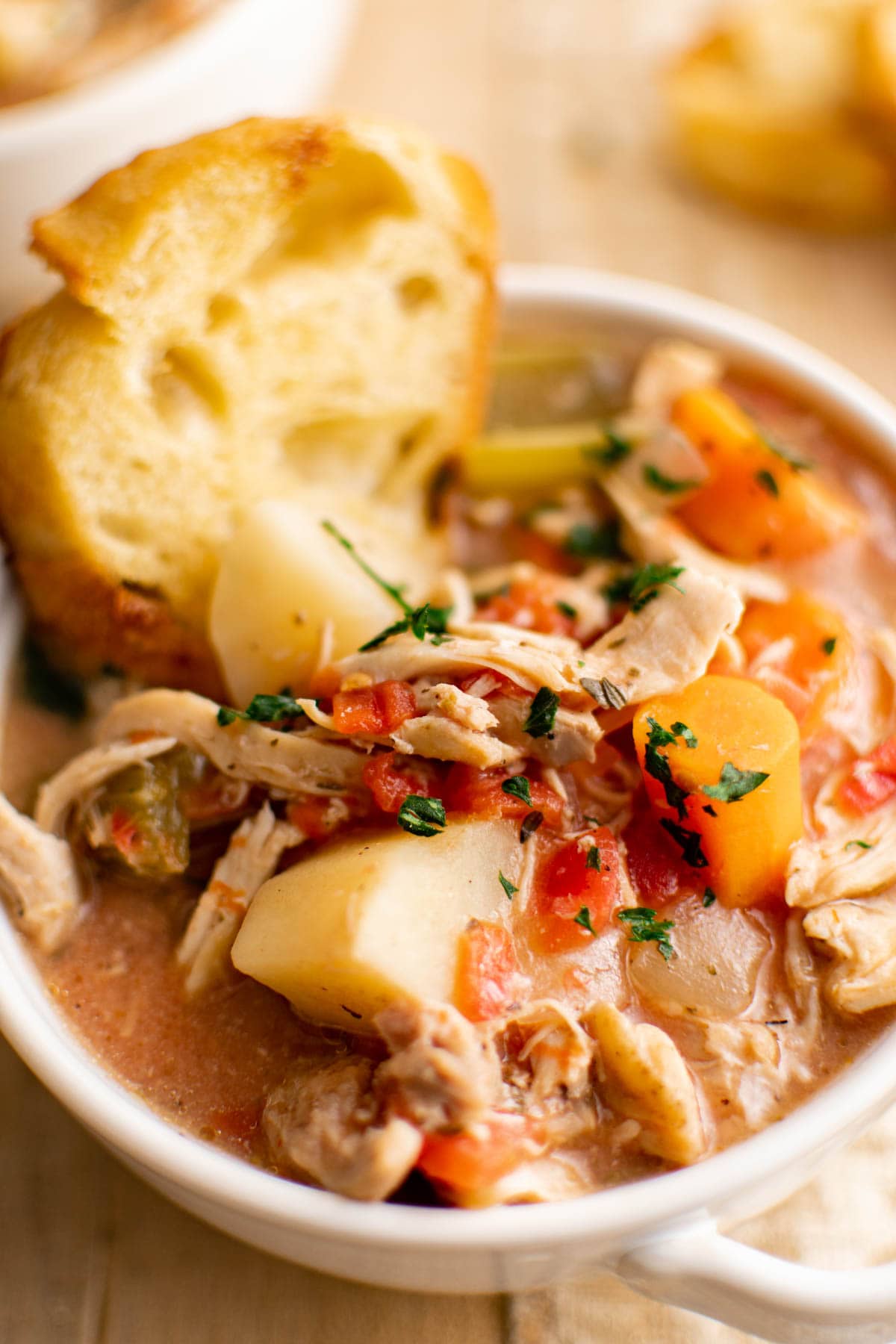 Bowl of chicken stew garnished with parsley and a piece of bread.