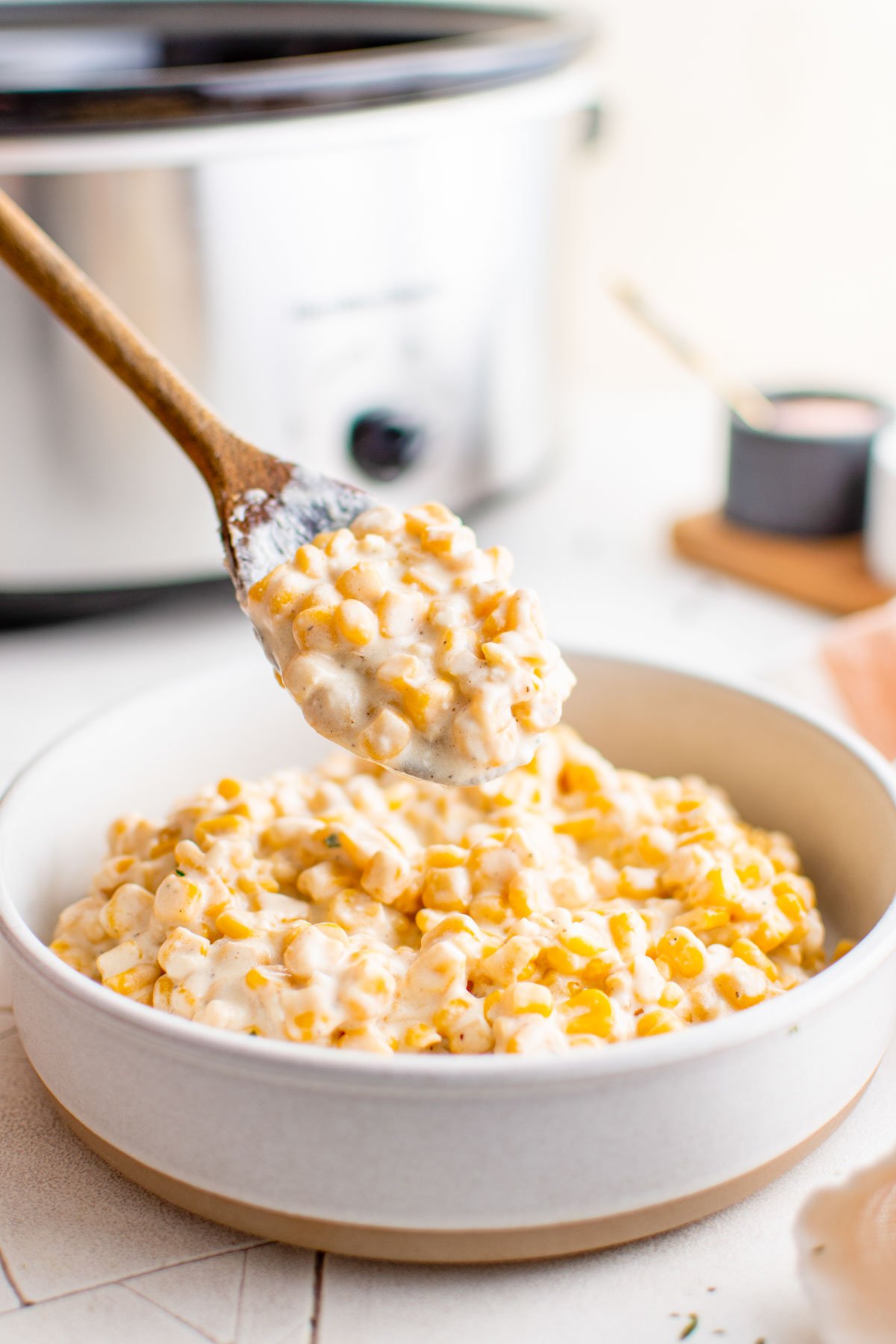 Cream corn, a wooden spoon and a large white serving bowl.