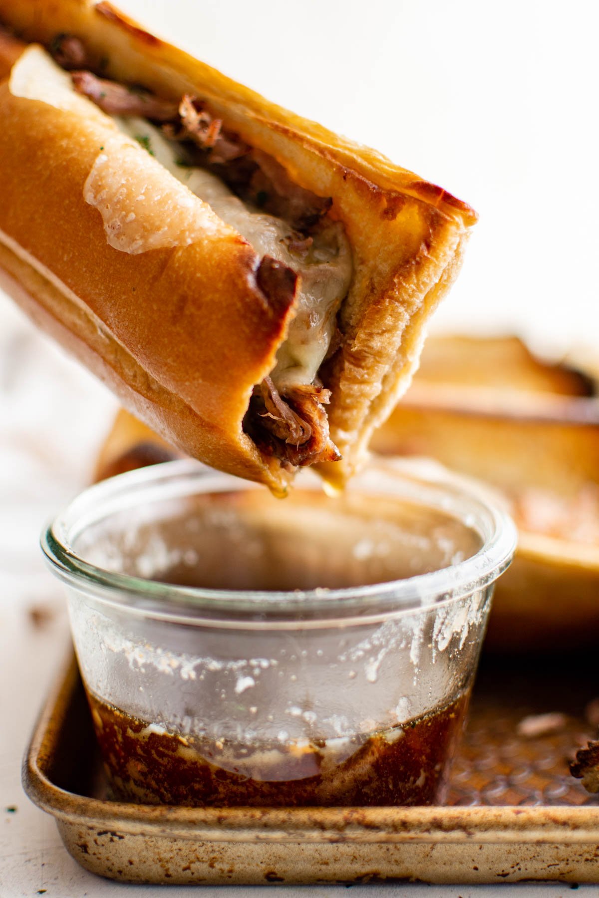 Beef sandwiches being dipped into a small cup of au jus.