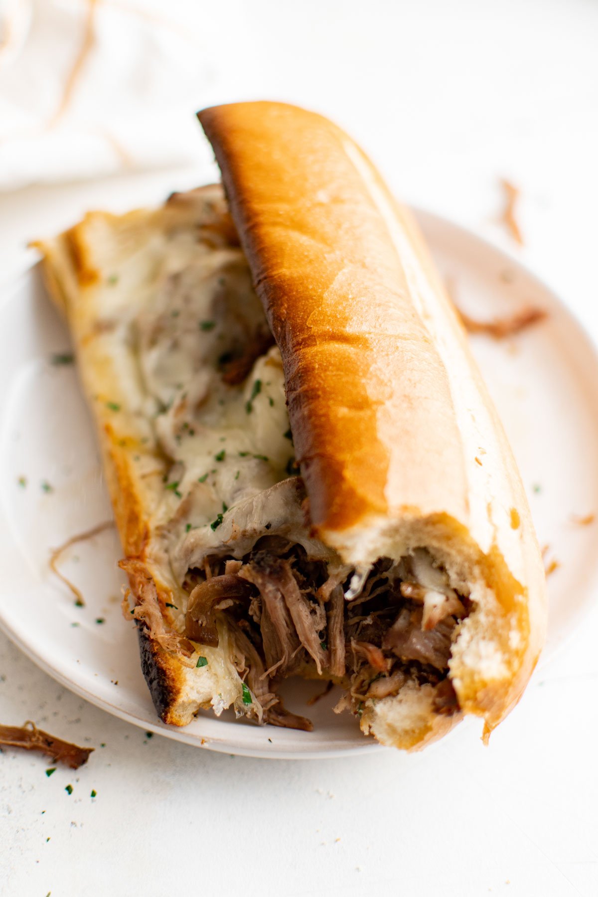 Shredded beef in a sandwich roll topped with cheese, with a bite taken out of it.