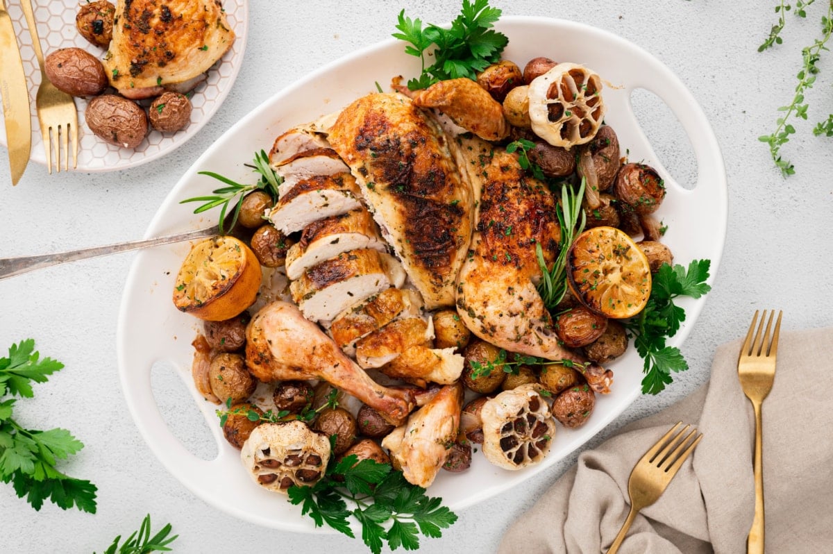 Roasted spatchcock chicken and potatoes on a white platter, with fresh parsley and herbs.