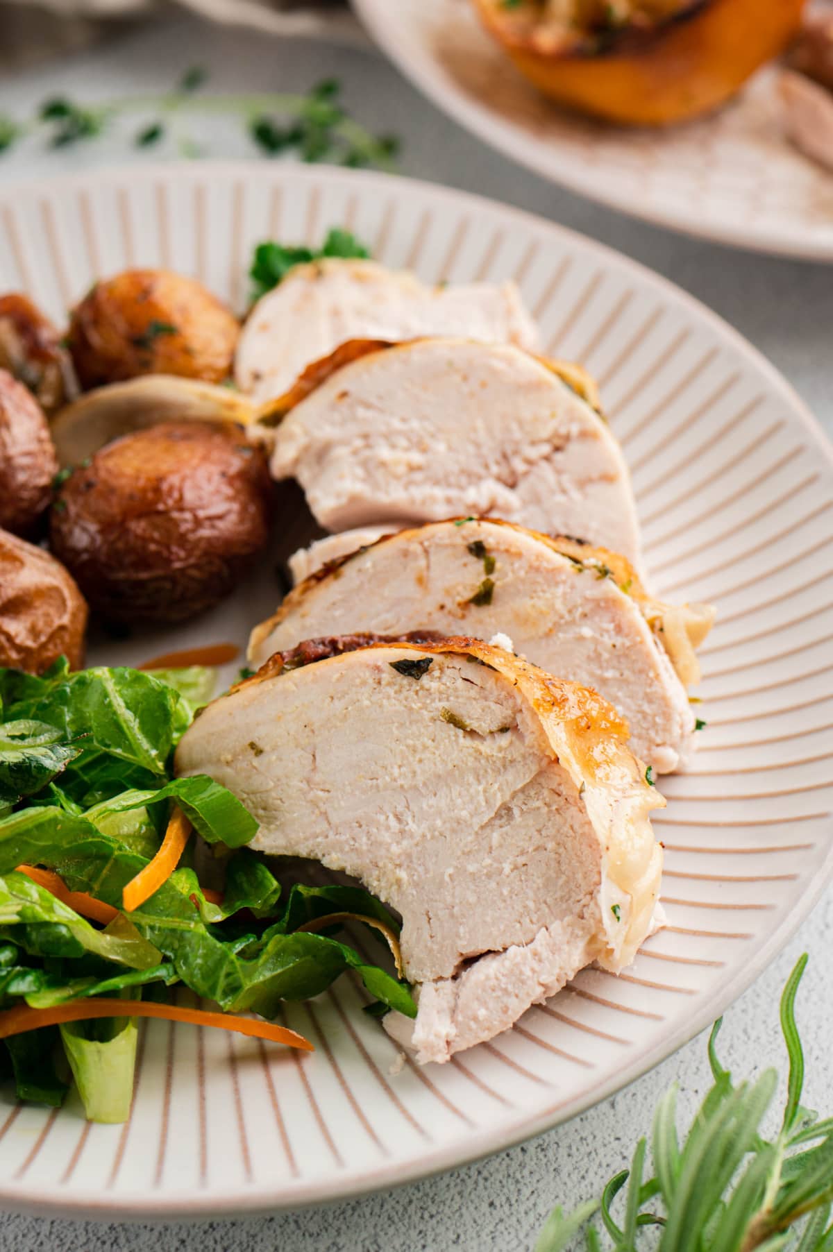 Sliced chicken breast on a plate with potatoes and salad greens.