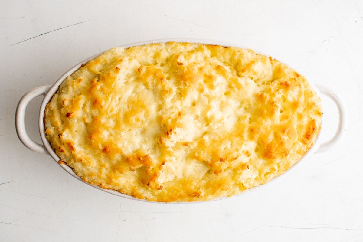 Cheesy mashed potatoes in a casserole dish, baked, with a golden top.