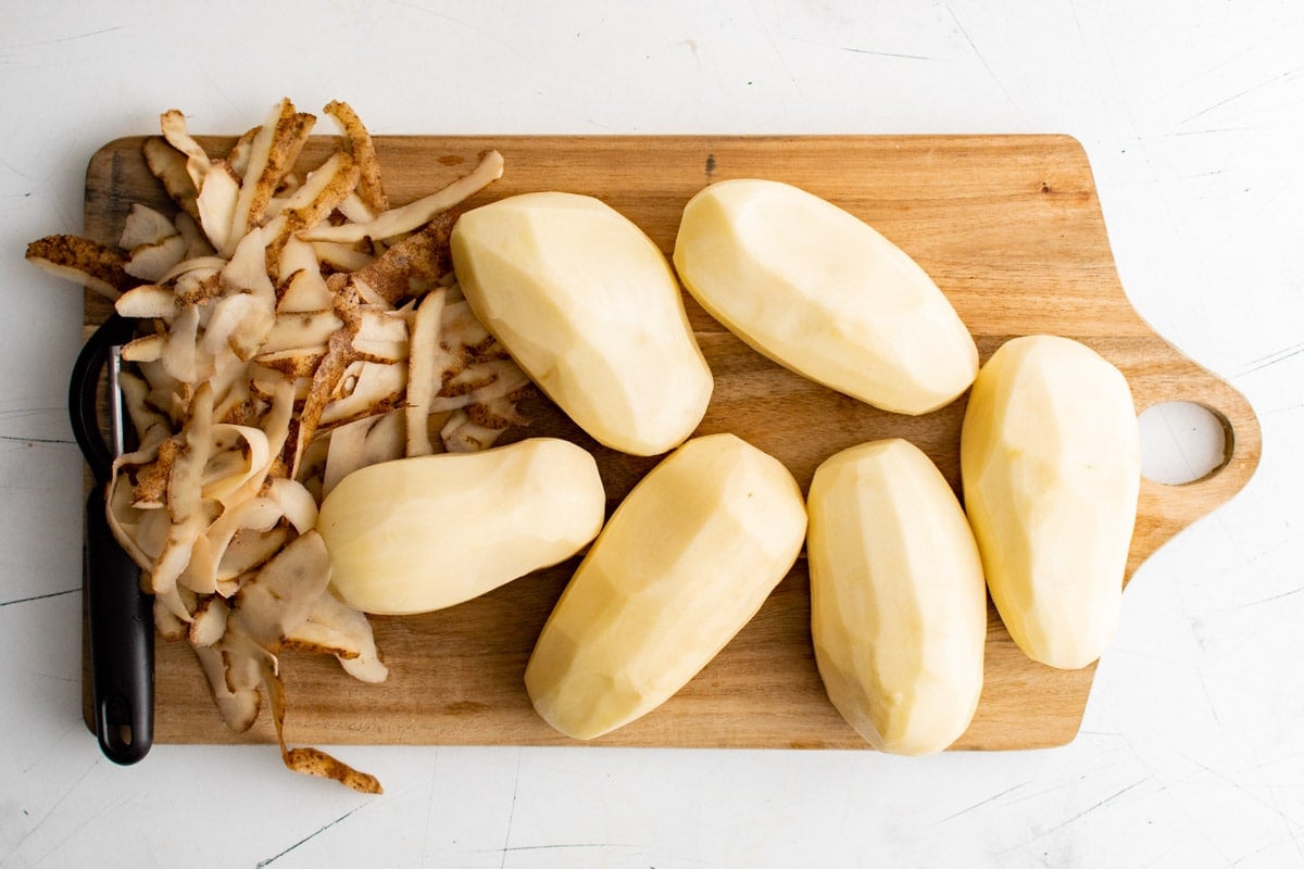 Russet potatoes, peeled, on a cutting board.