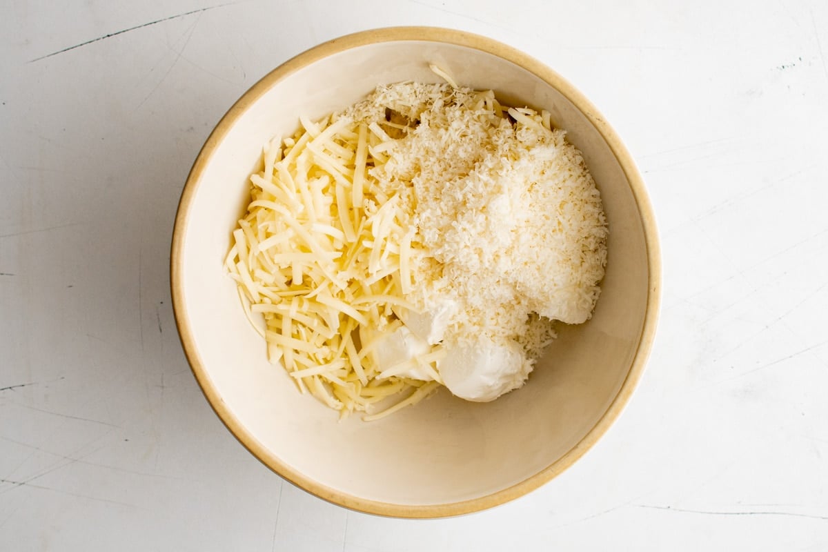 Shredded white cheddar cheese, Parmesan and cream cheese in a large bowl.