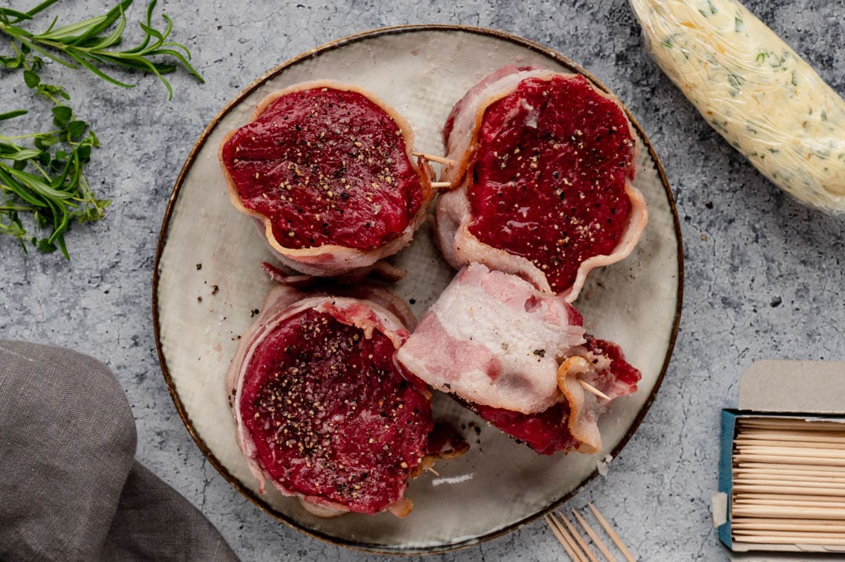 Filet mignon steaks wrapped with bacon, sitting on.a plate.