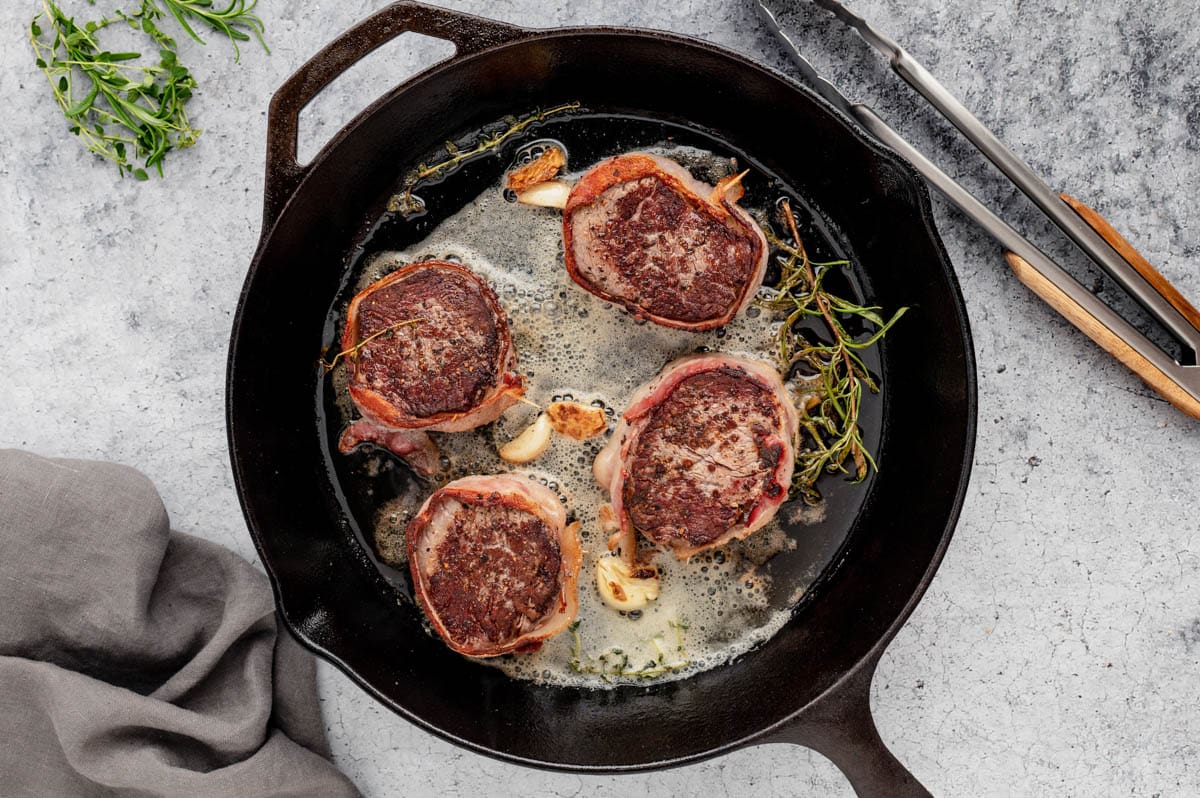 Bacon wrapped filet mignon steaks in a cast iron skillet with melted butter, garlic and fresh rosemary.