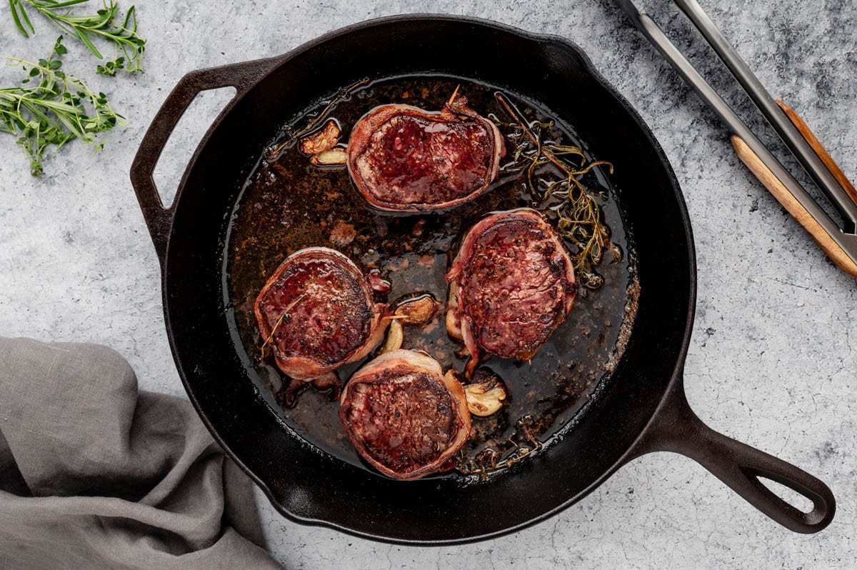 Filet mignon steaks in a cast iron skillet with roasted garlic.