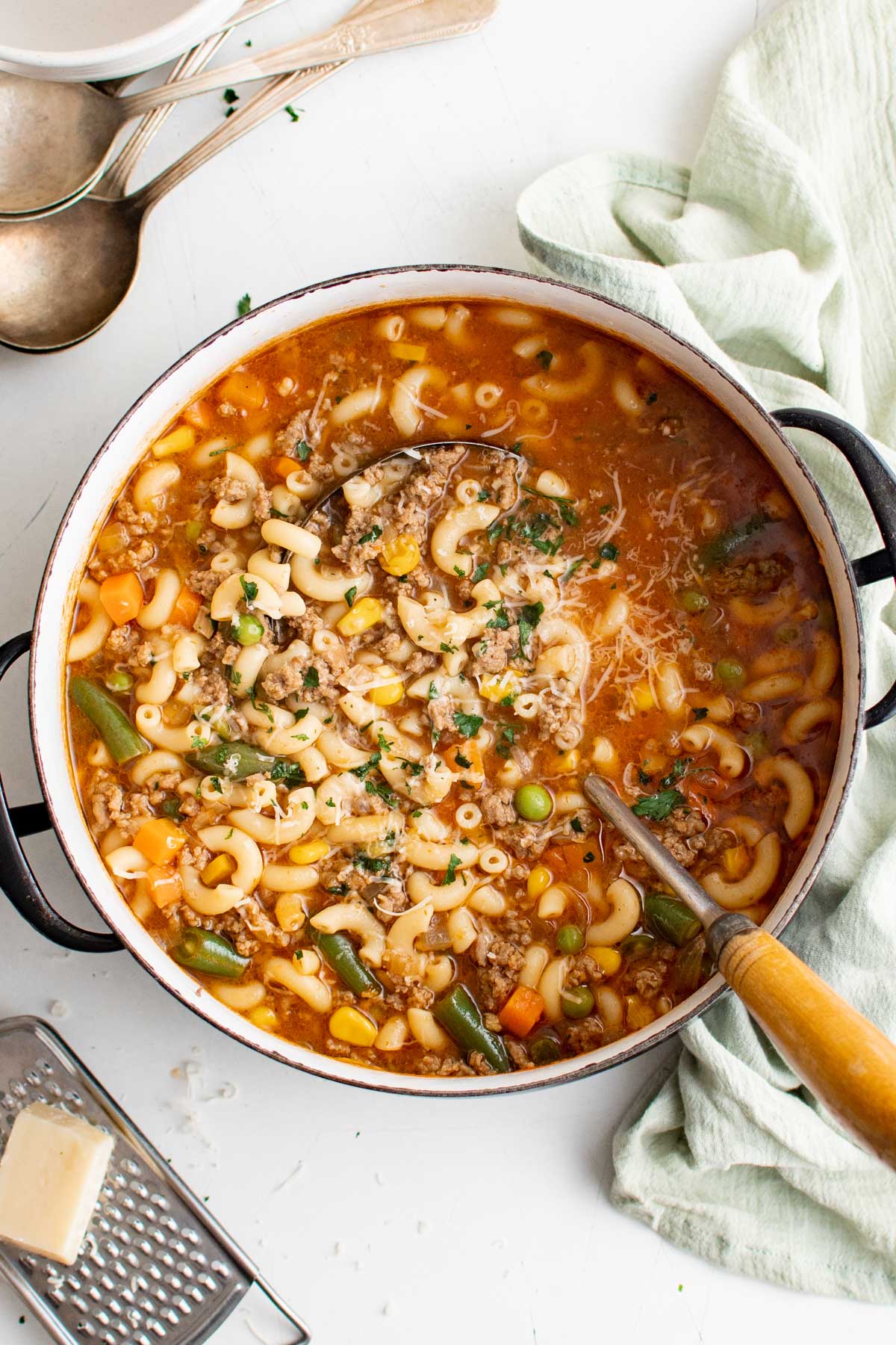 Soup pot filled with soup with hamburger, macaroni and vegetables and a ladle.