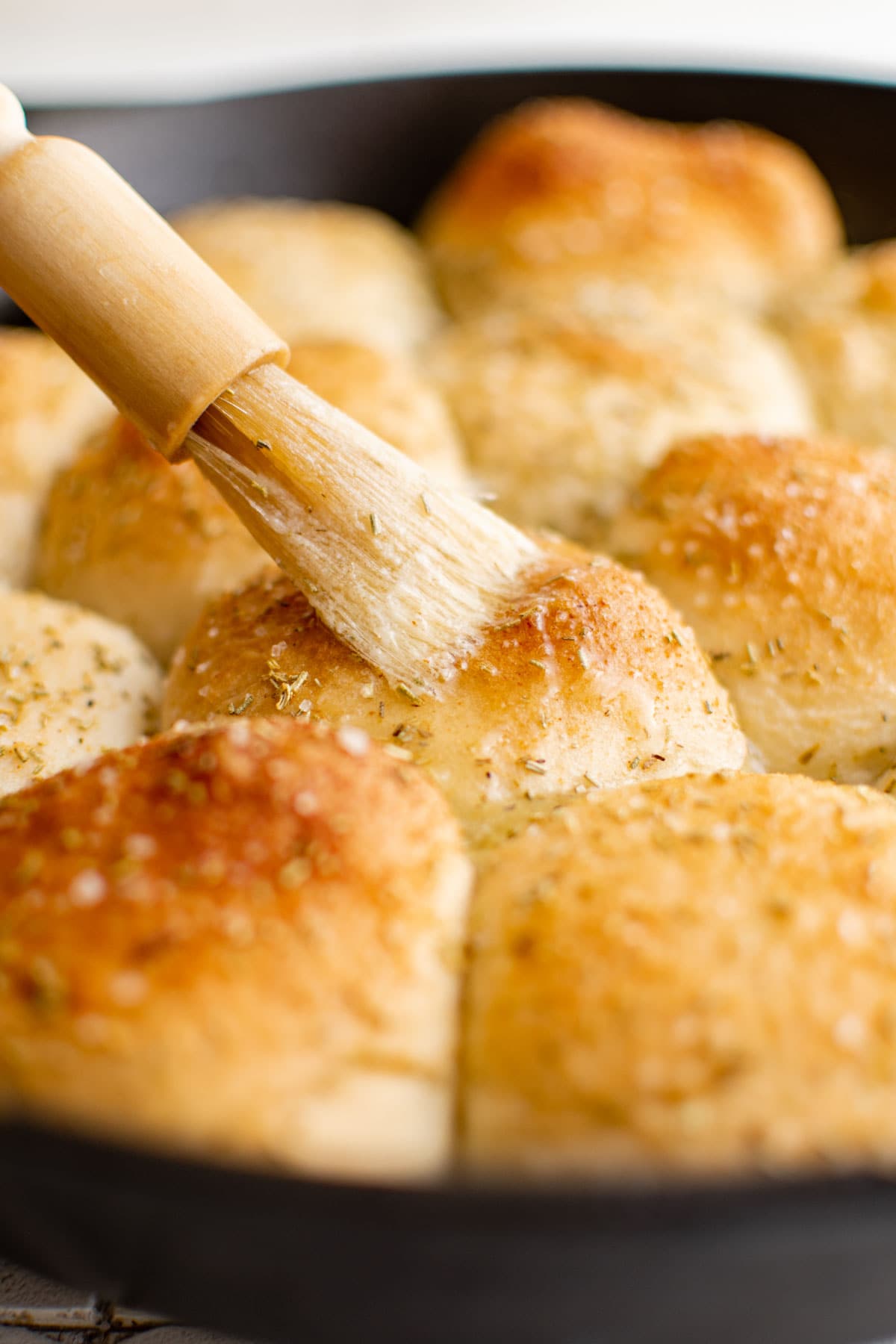 Baked frozen dinner rolls in a skillet with a pastry brush and butter. 