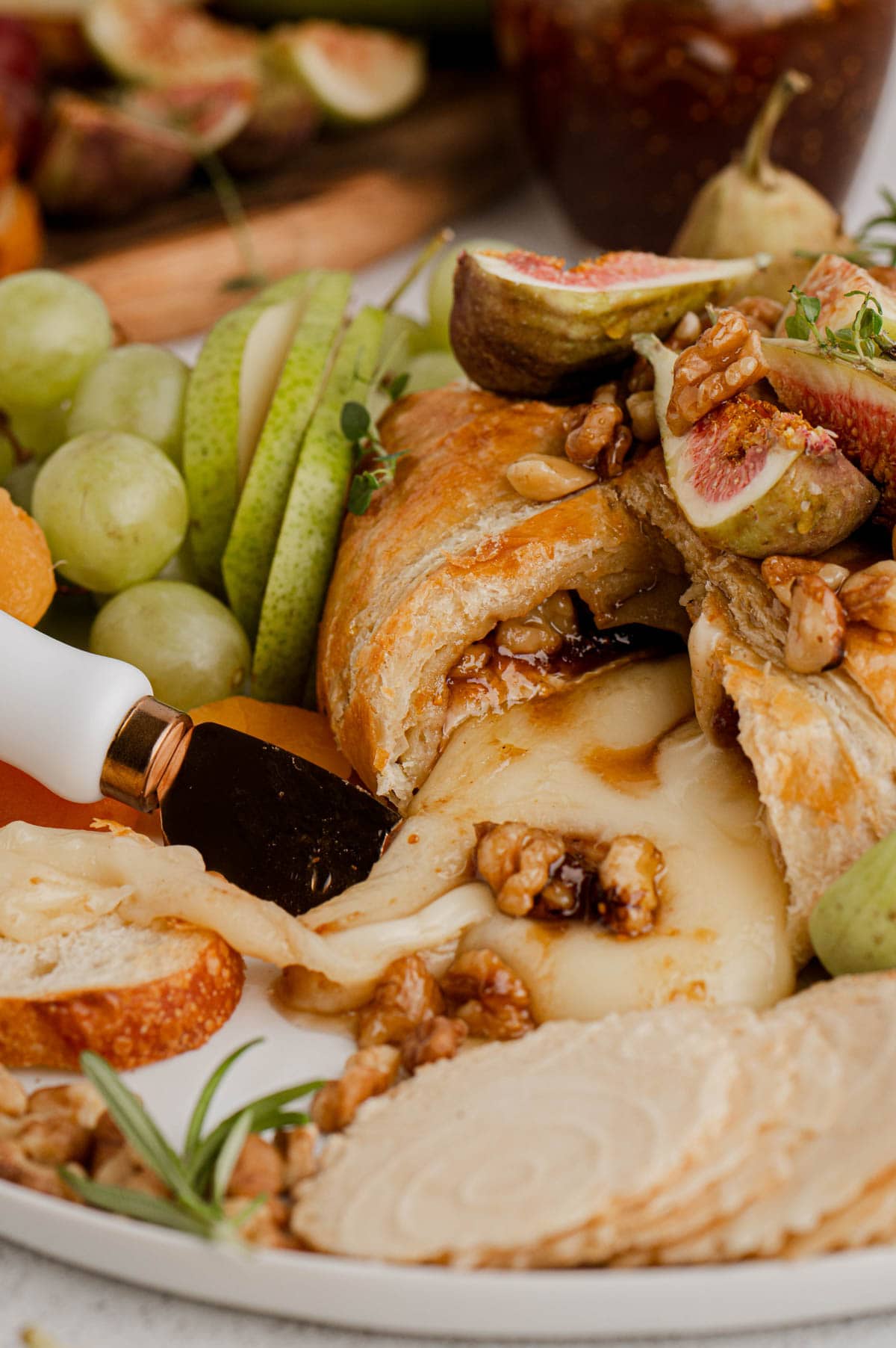 Brie cheese malting out of a puff pastry shell, surrounded by sliced apples, grapes, and crackers.