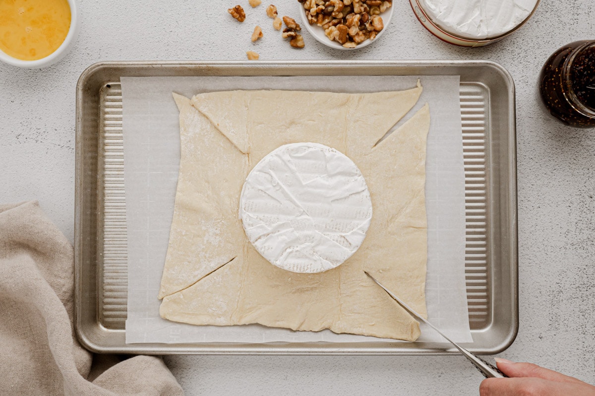 Puff pastry rolled out on a baking sheet with a wheel of Brie cheese.