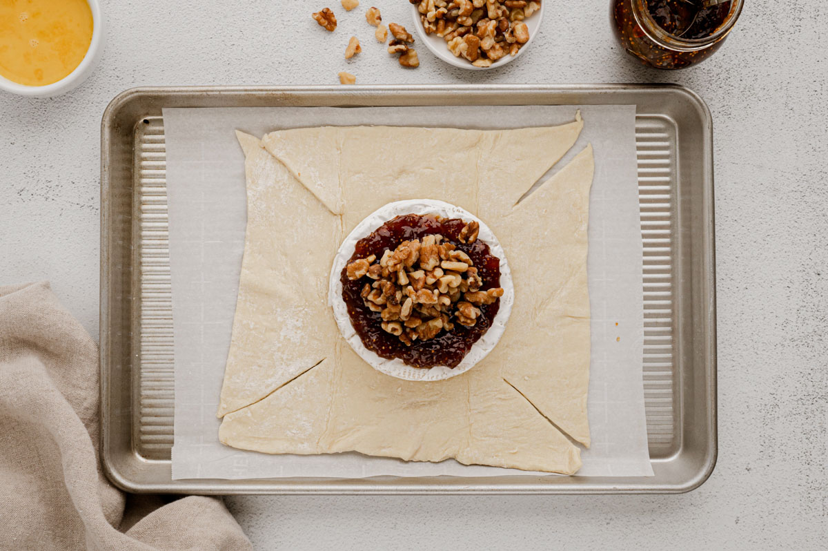 Puff pastry rolled out on a baking sheet with a wheel of Brie cheese topped with fig jam and walnuts.