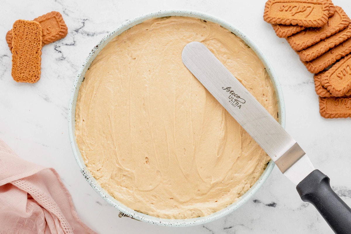 Flat spatula spreading cheesecake batter in a springform pan.