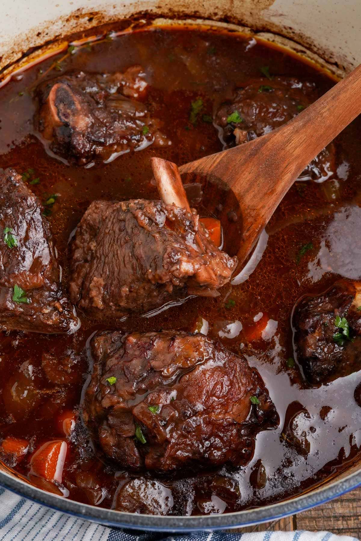 Braised beef short ribs in a large dutch oven with a wooden spoon.