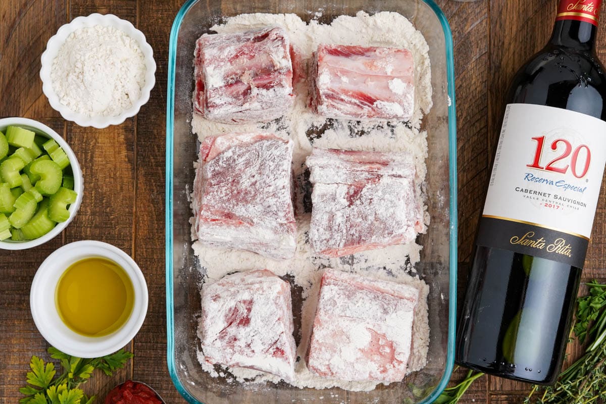 Beef short ribs coated with flour in a glass baking dish.