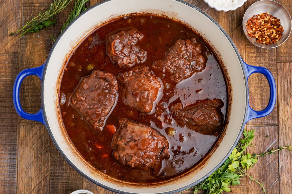 Red winge sauce and beef short ribs simmering a large pot.