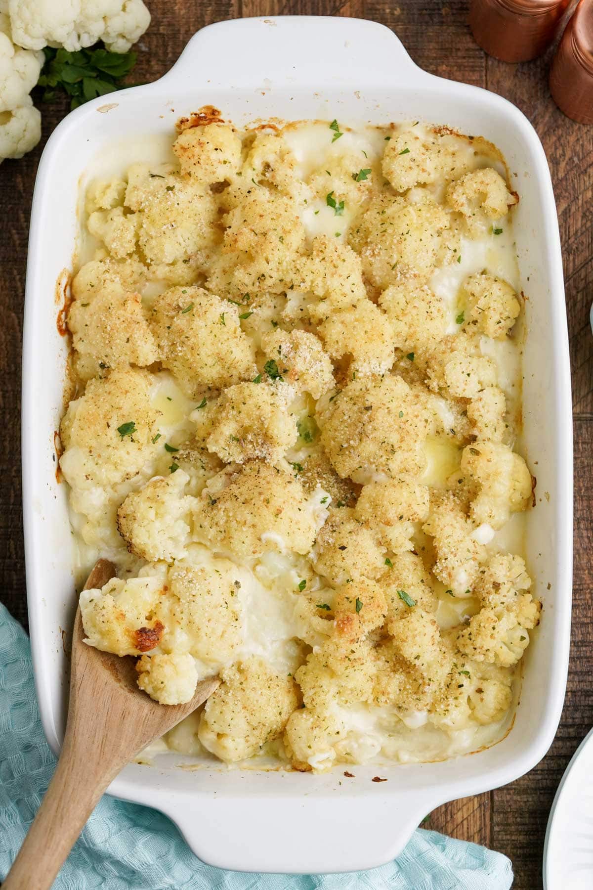 Baked cauliflower in cheese sauce with breadcrumbs and a wooden spoon.