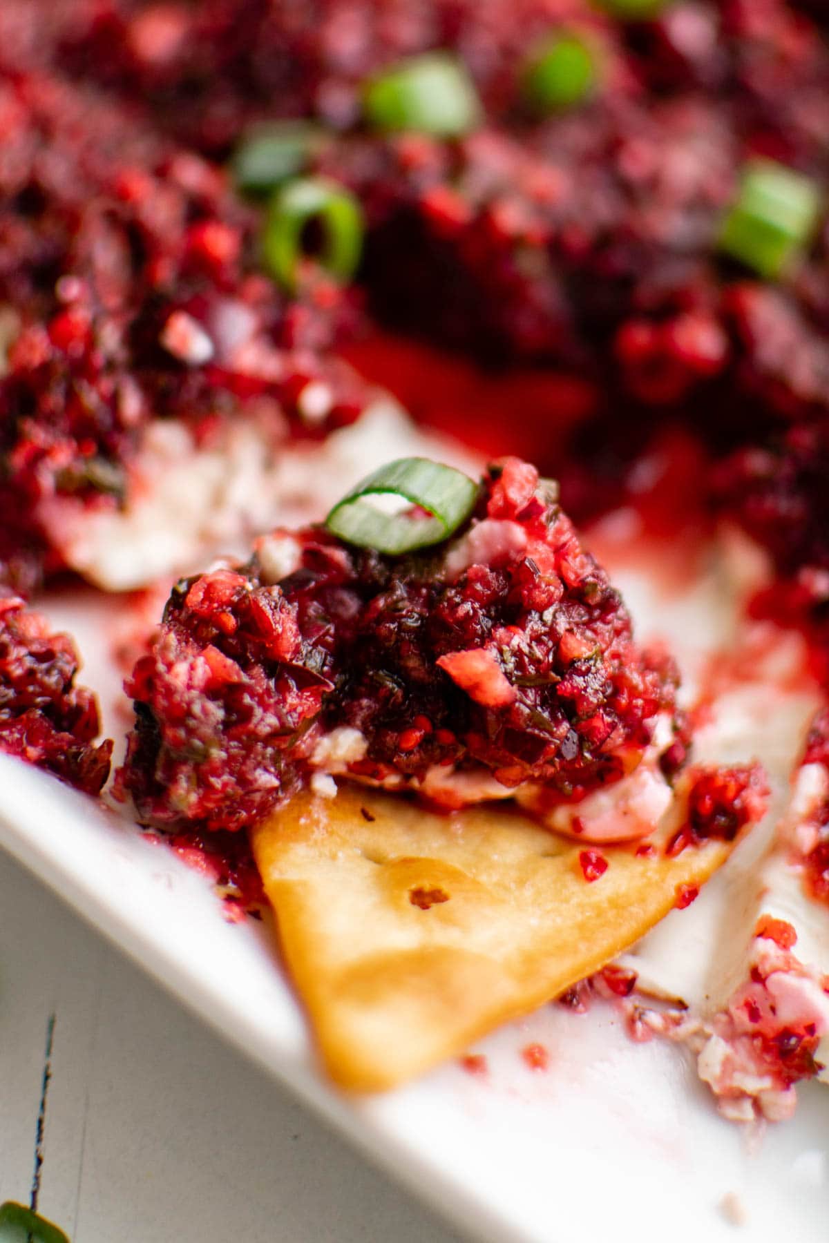 A cracker dipped into cranberry jalapeno dip.