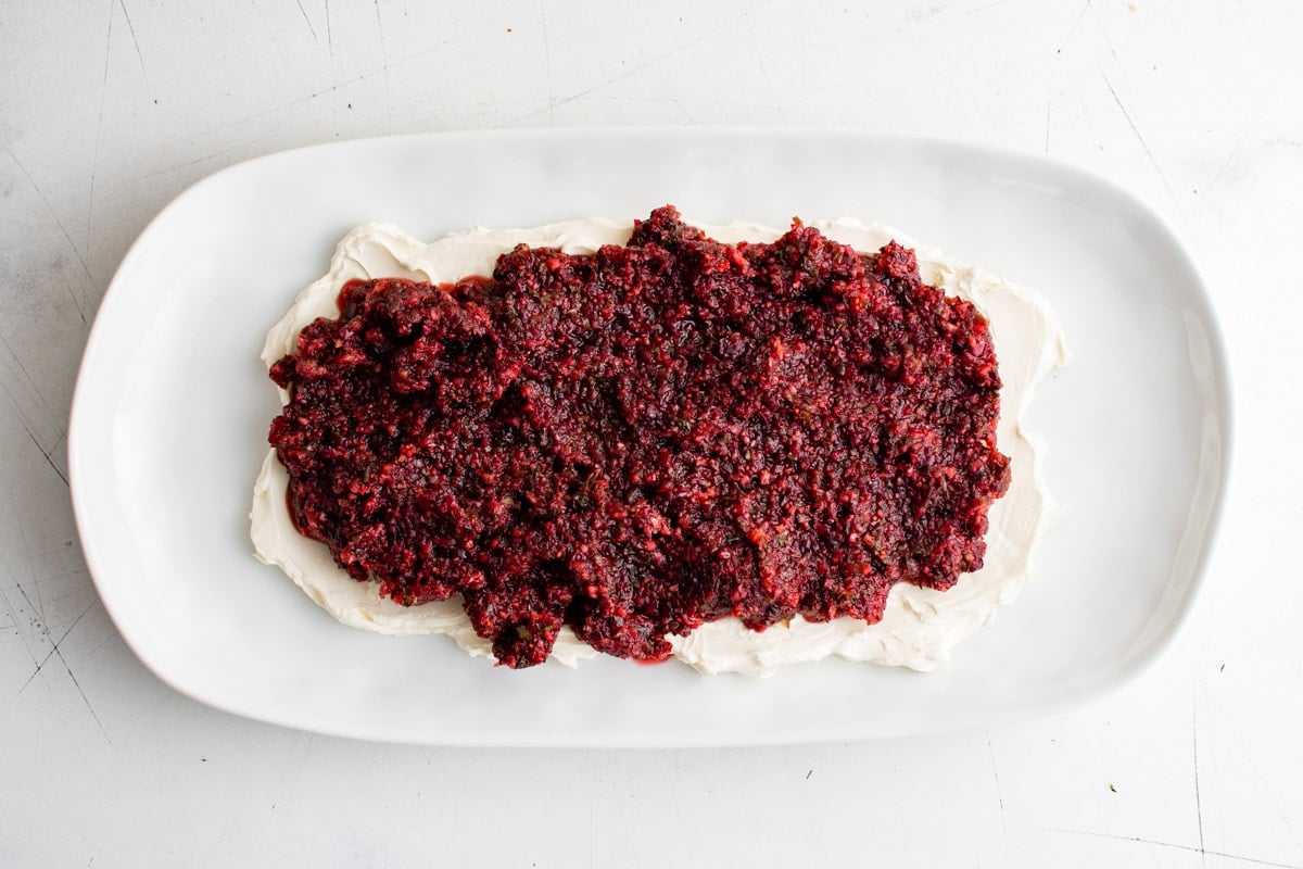 Cream cheese spread on a large white platter with cranberry relish on top.