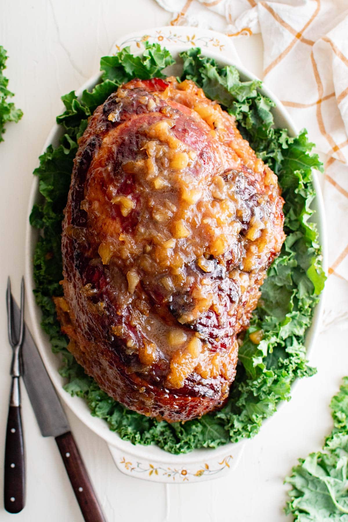 Glazed ham on a bed of kale in a white platter.