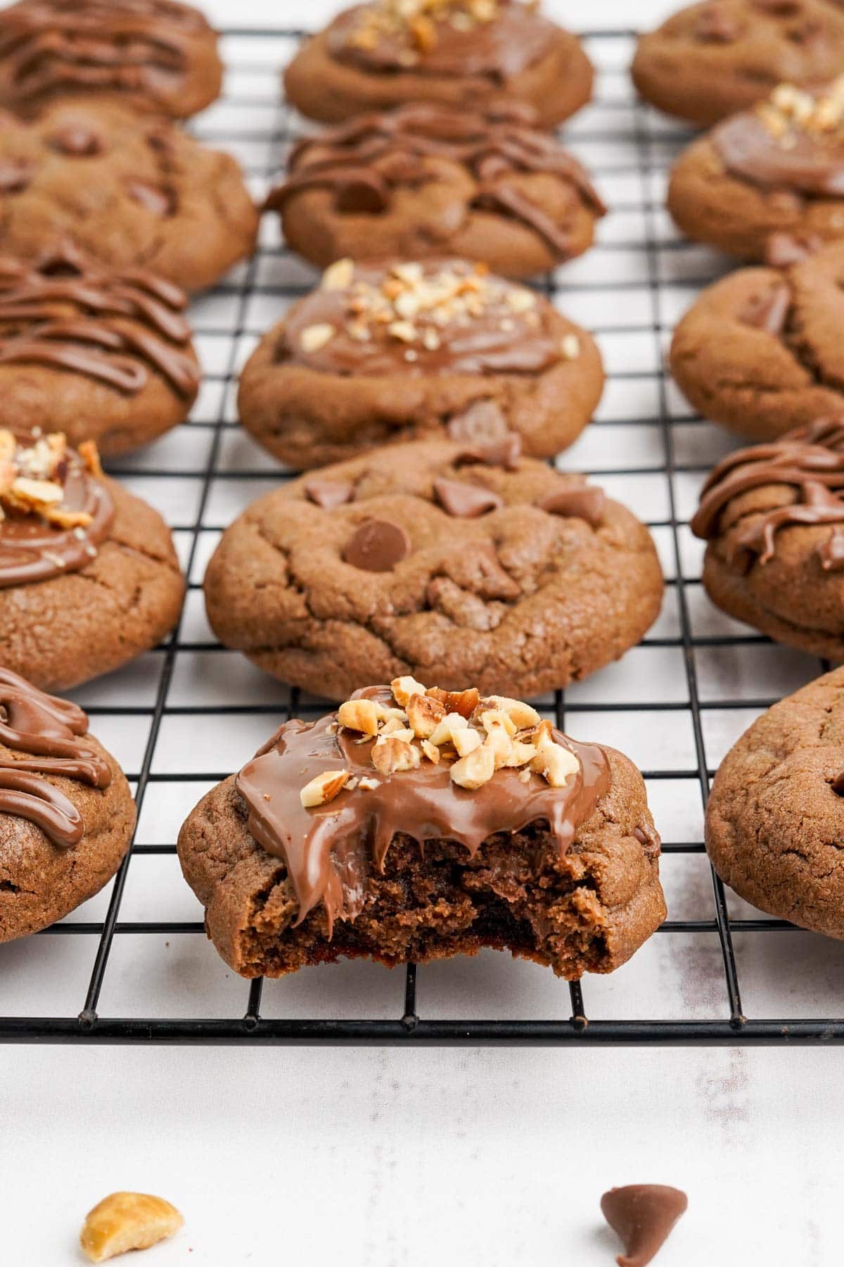 Wire cooling rack with nutella cookies with frosting, hazelnuts and chocolate chips.