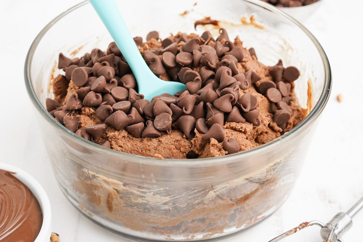 Chocolate chips and a bowl of cookie dough and a blue spatula.