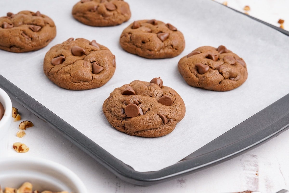 Chocolate cookies on a baking sheet, topped with chocolate chips.