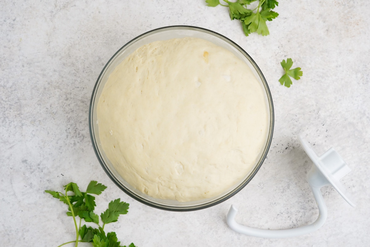 Risen dough in a large clear glass mixing bowl.