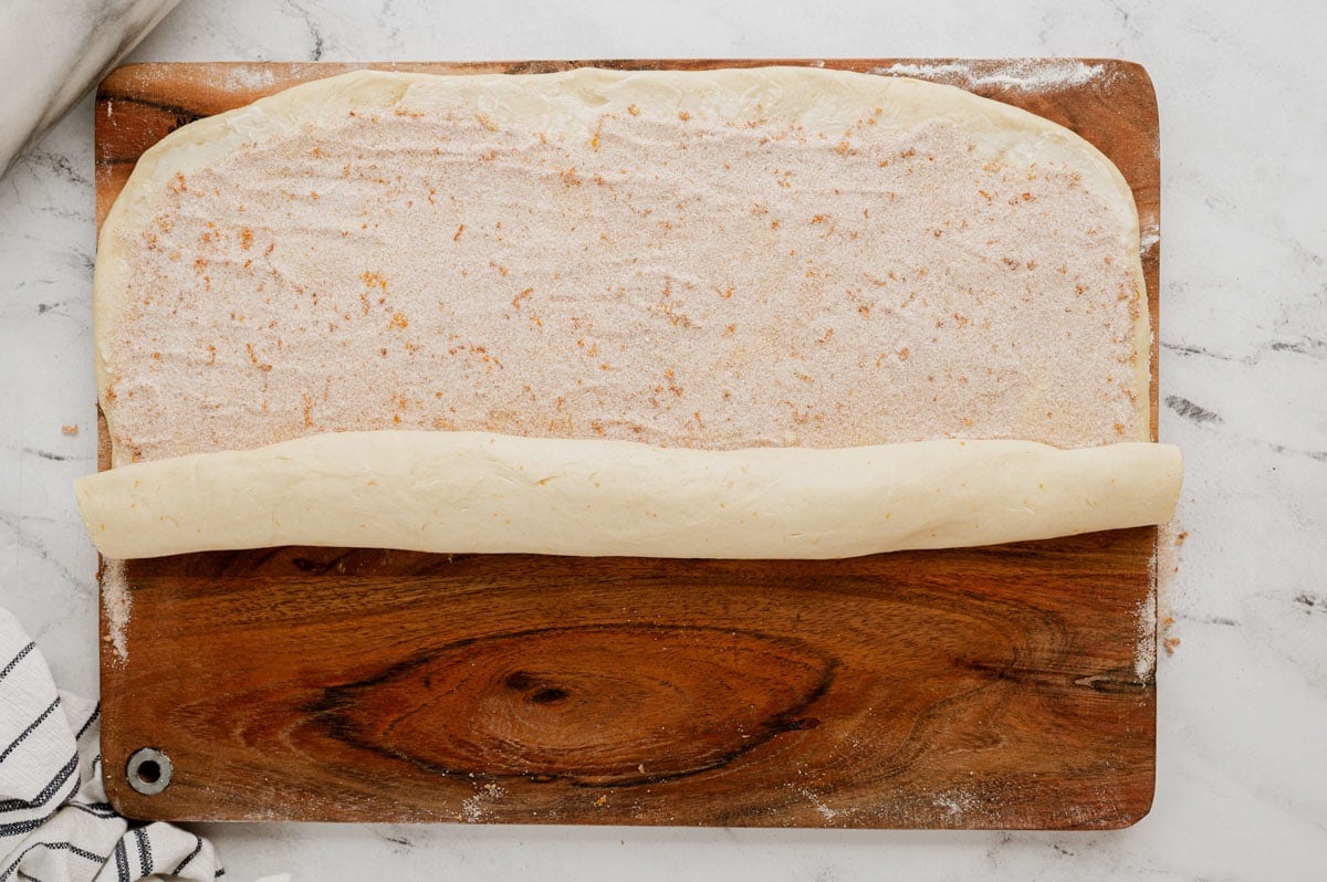 Cinnamon sugar filling on flatteded dough, rolled at one side.