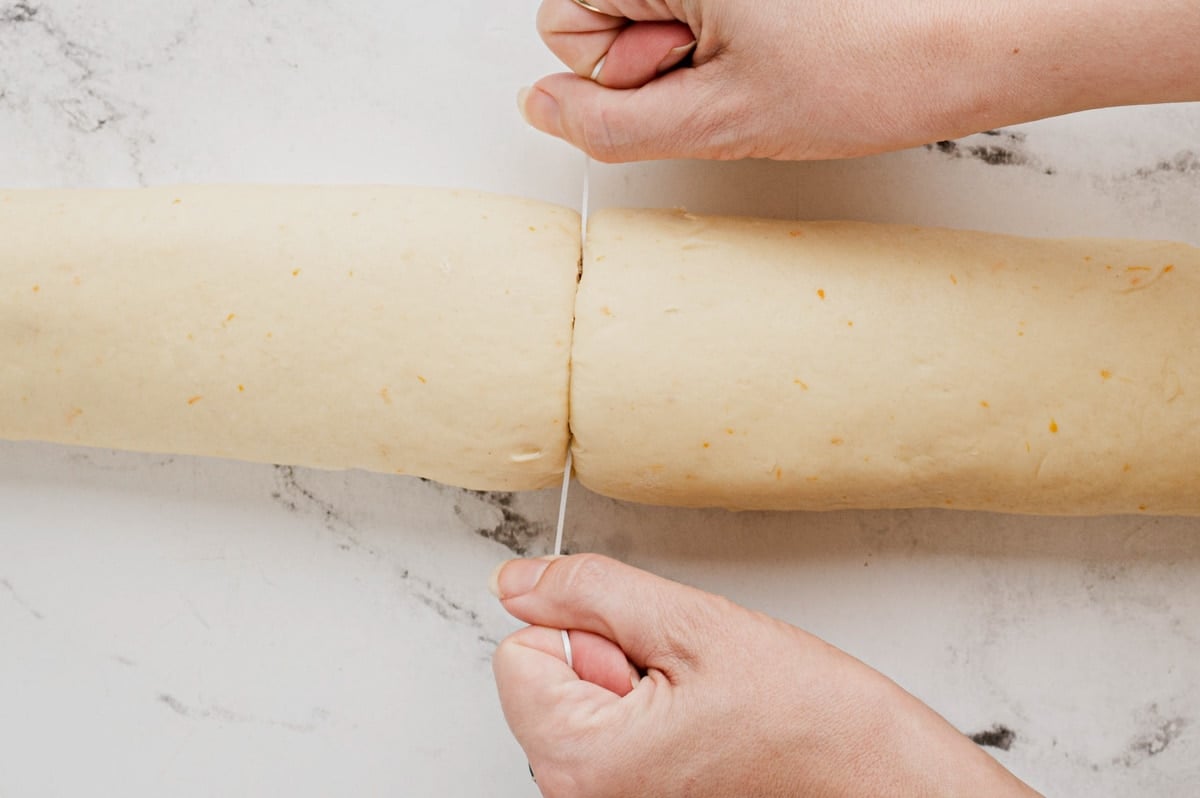 Rolled up dough, hands using dental floss to slice the roll into pieces.