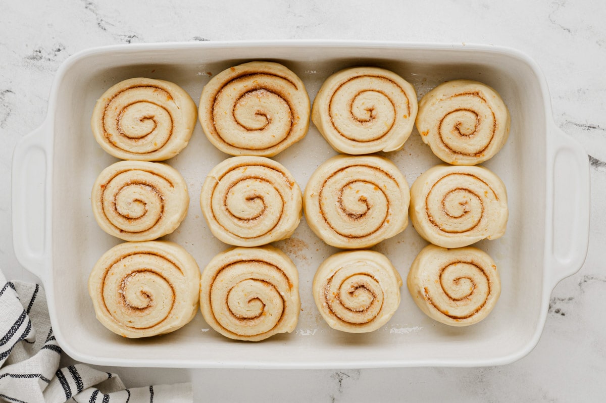 Orange rolls in a baking dish to rise.